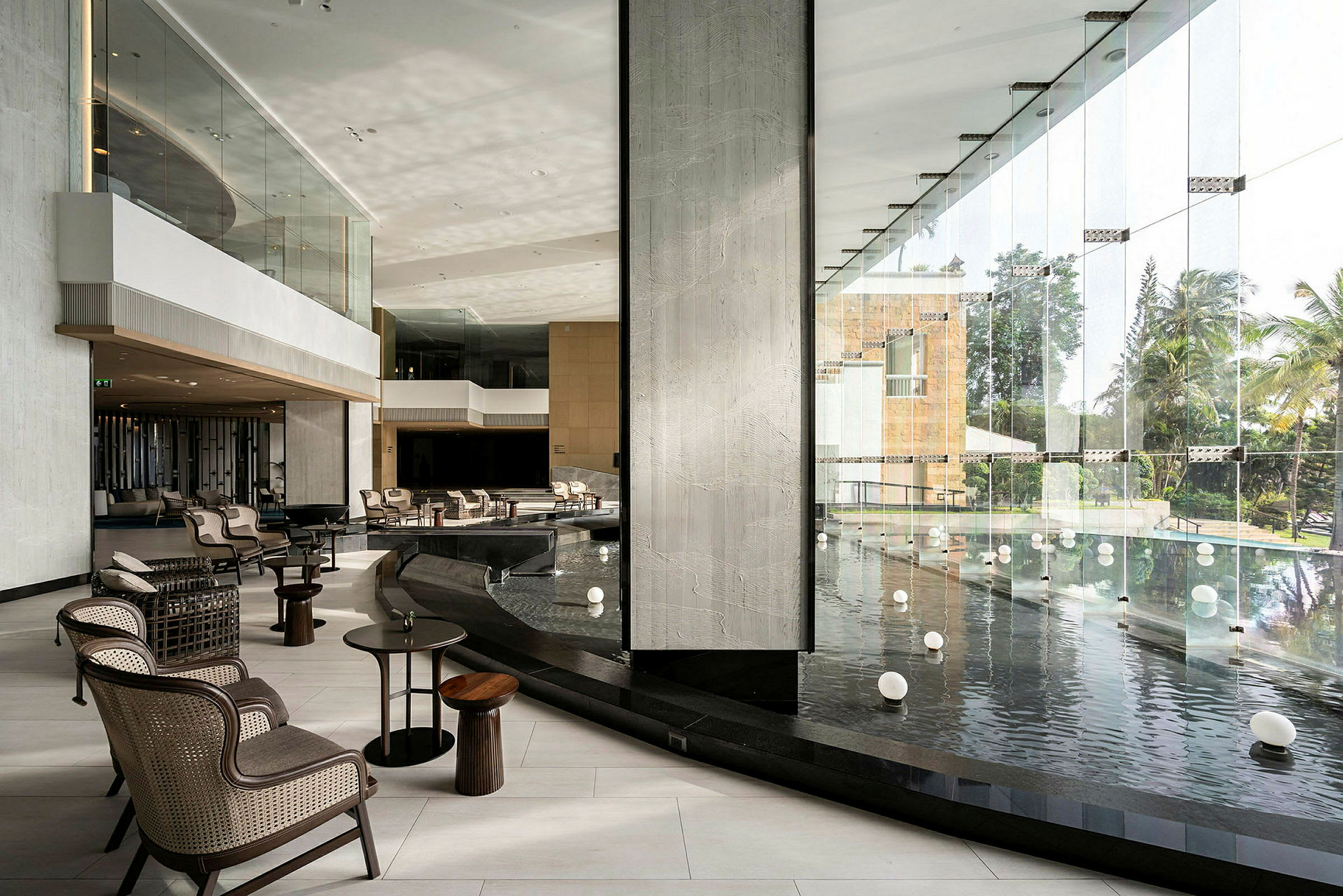 En hotellobby med store glasvægge, der vender ud mod en pool med flydende dekorative kugler. Flere siddepladser med borde og stole er synlige i et moderne indendørsmiljø. (AI-genereret tekst)
