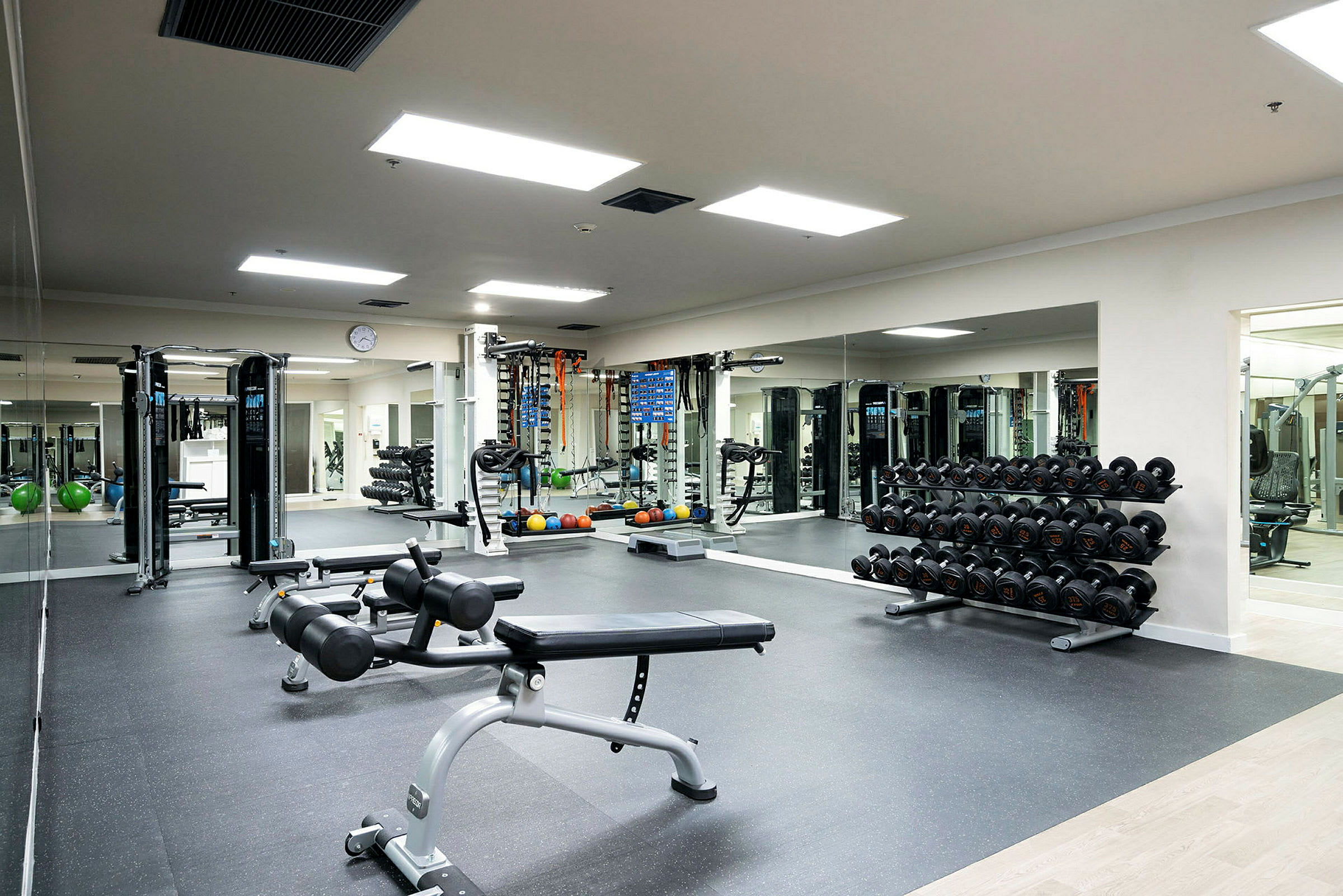 Et fitnesscenter med frie vægte, træningsmaskiner og træningsbænke, med spejlvægge og lyse lofter i baggrunden. (AI-genereret tekst)