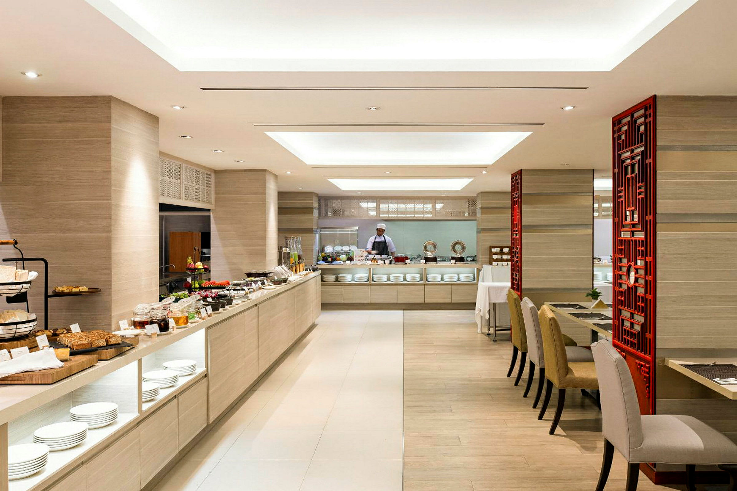 En lys restaurant med en stor buffet fuld af mad og en kok i baggrunden. (AI-genereret tekst)