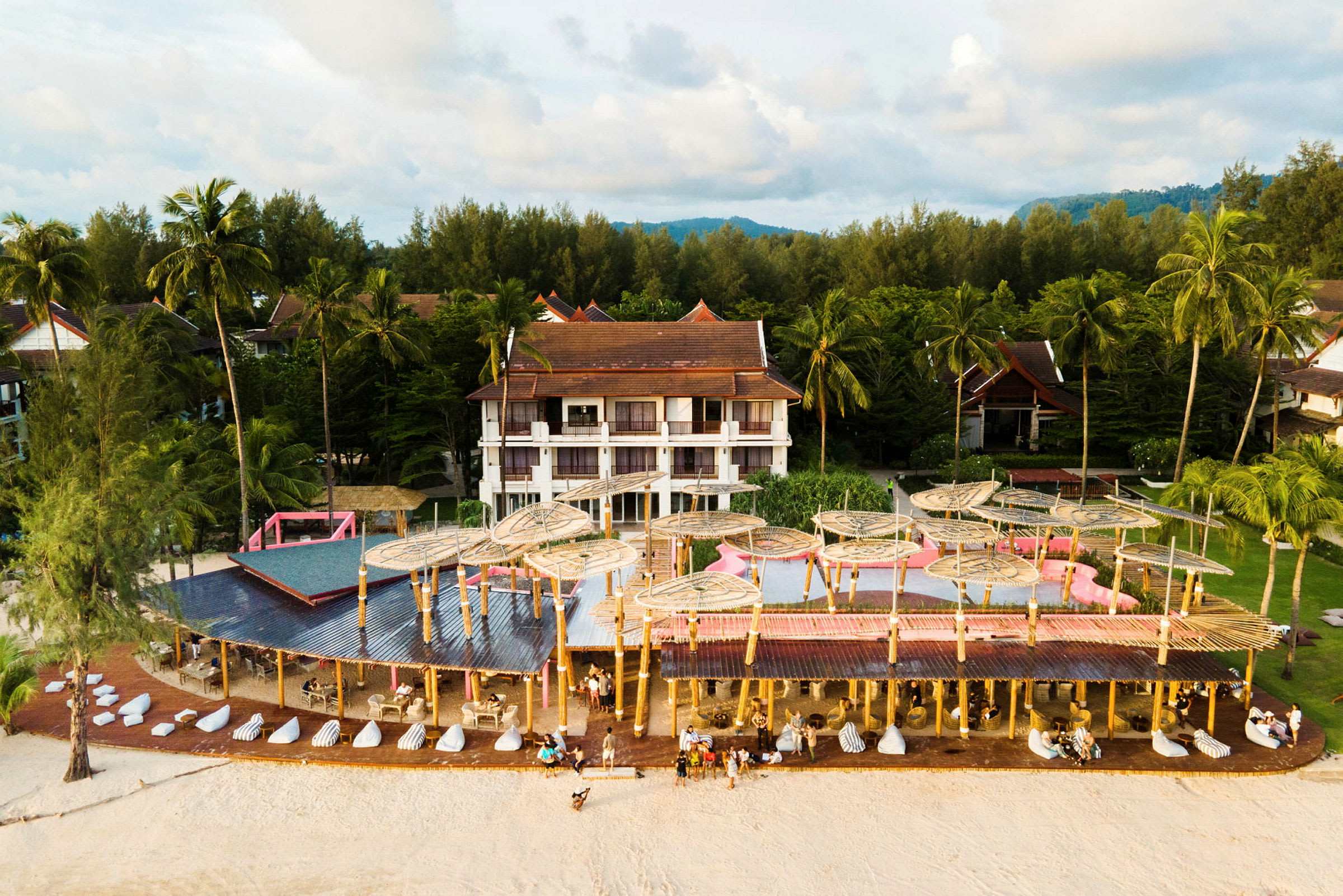 Hotellets bygninger omgivet af palmer og et udendørs poolområde tæt på stranden. (AI-genereret tekst)