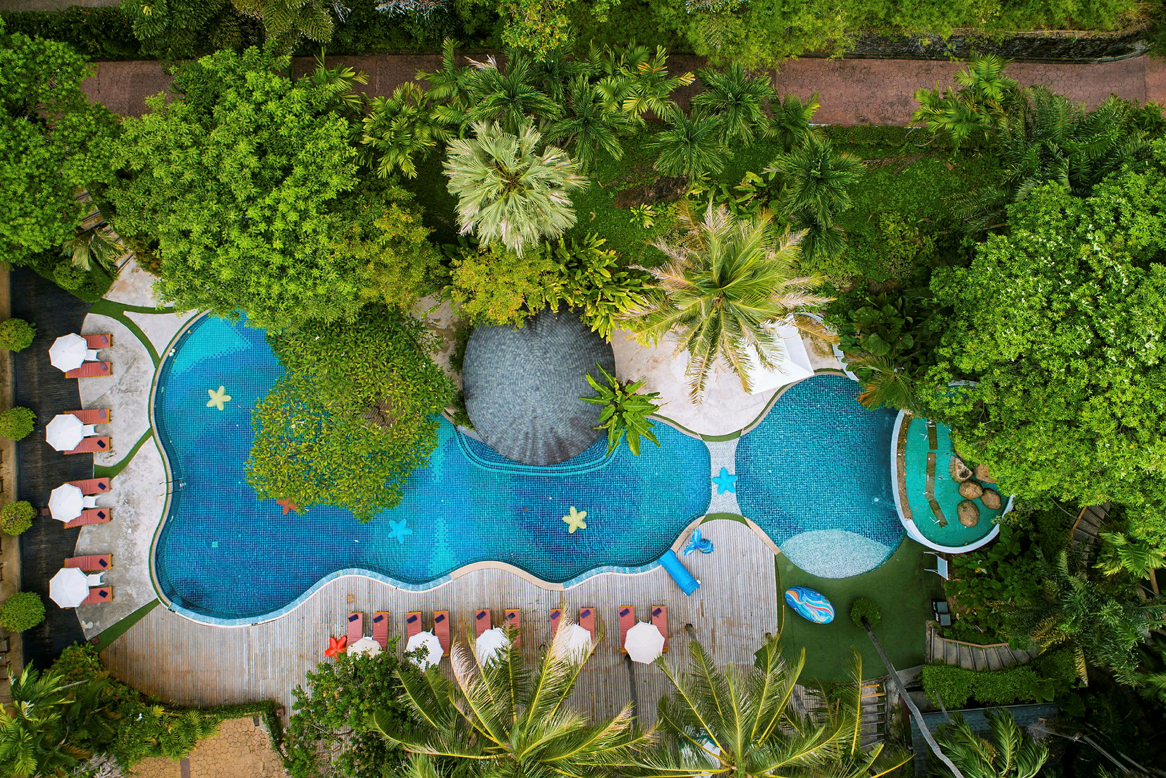 Luftfoto af en formet pool, omgivet af liggestole og vegetation. (AI-genereret tekst)