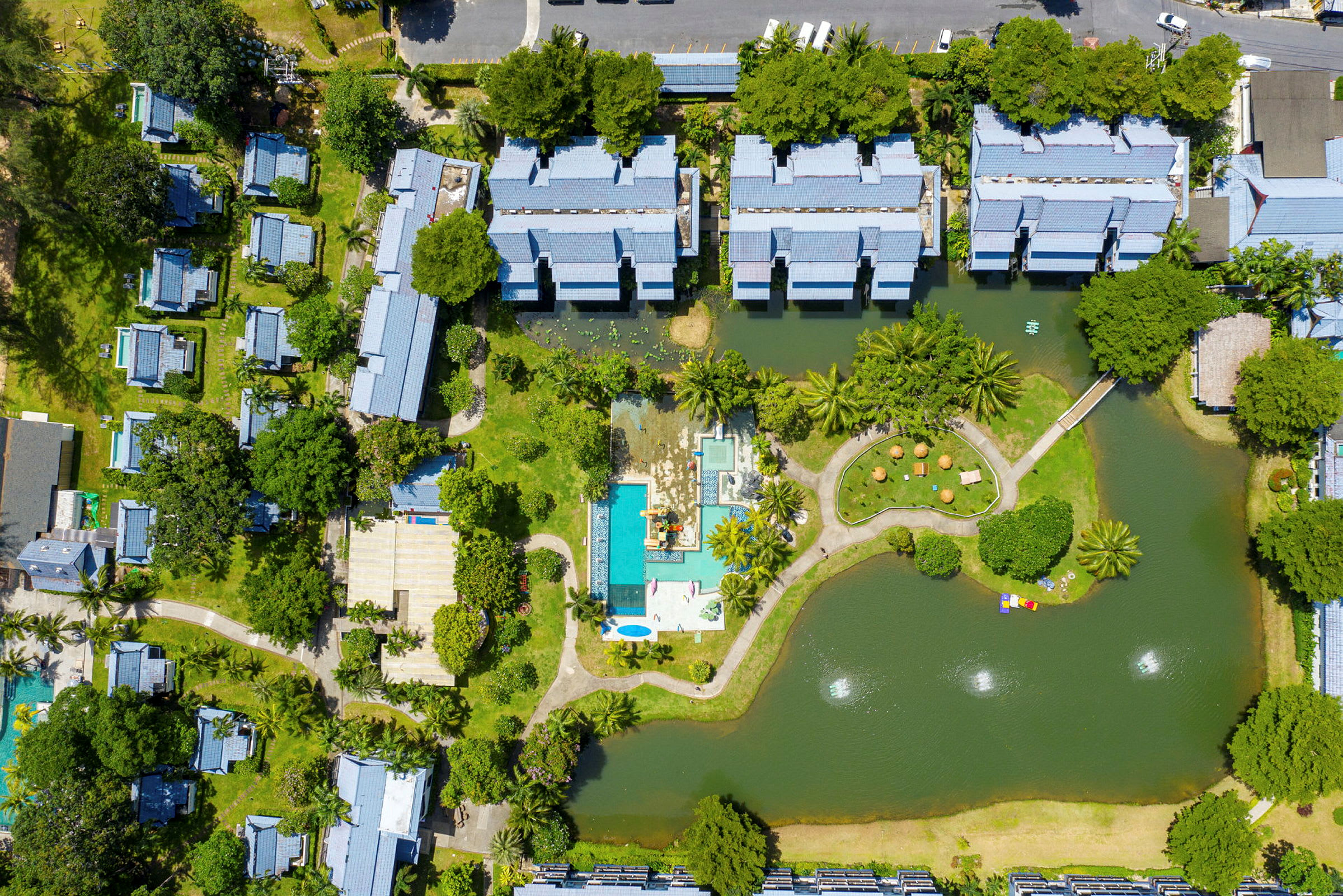 Luftfoto af en resort med bygninger, poolområde og omkringliggende grønne områder. (AI-genereret tekst)