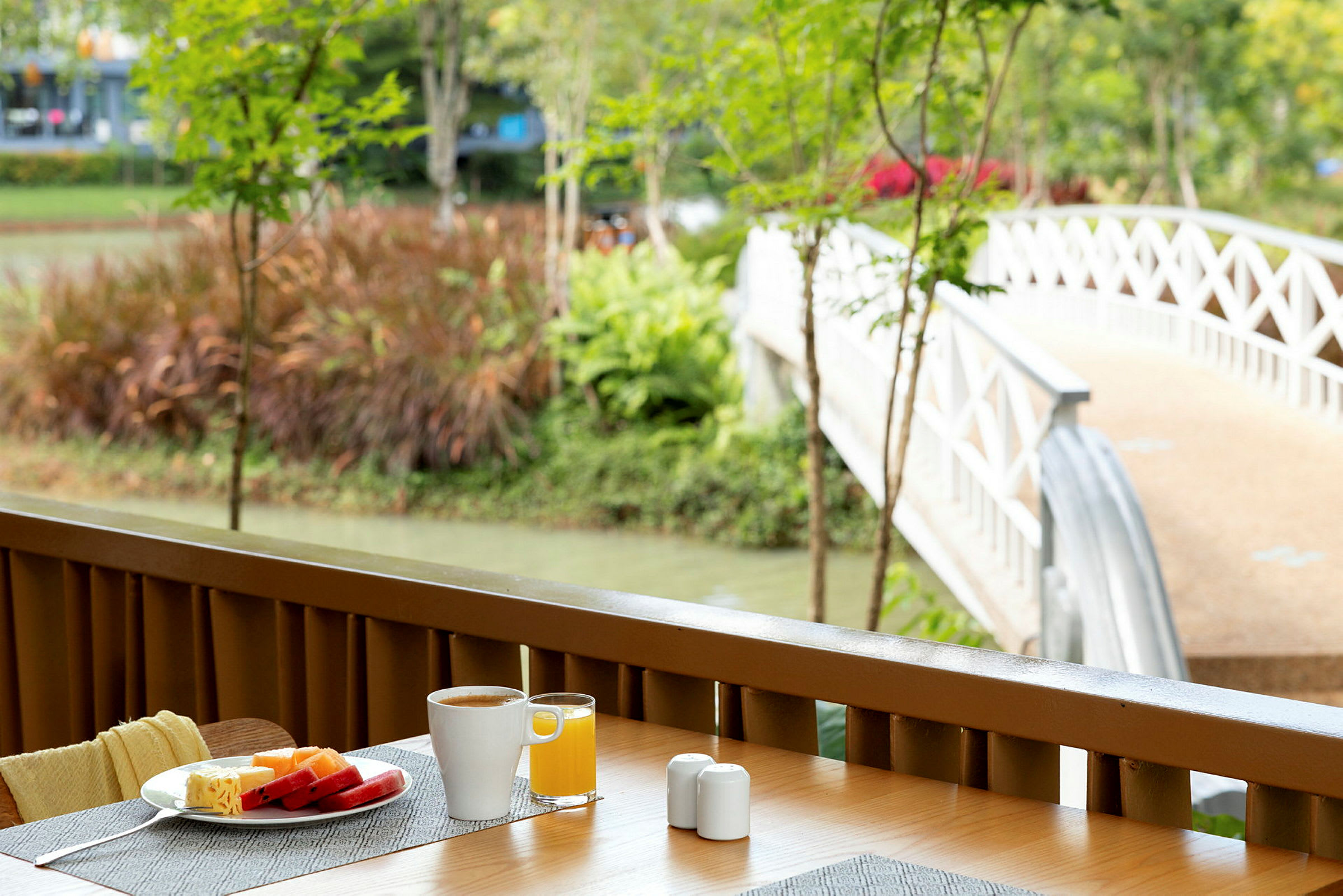 Morgenbord med kaffe og juice på en terrasse med udsigt til en hvid bro, der fører over en kanal. (AI-genereret tekst)