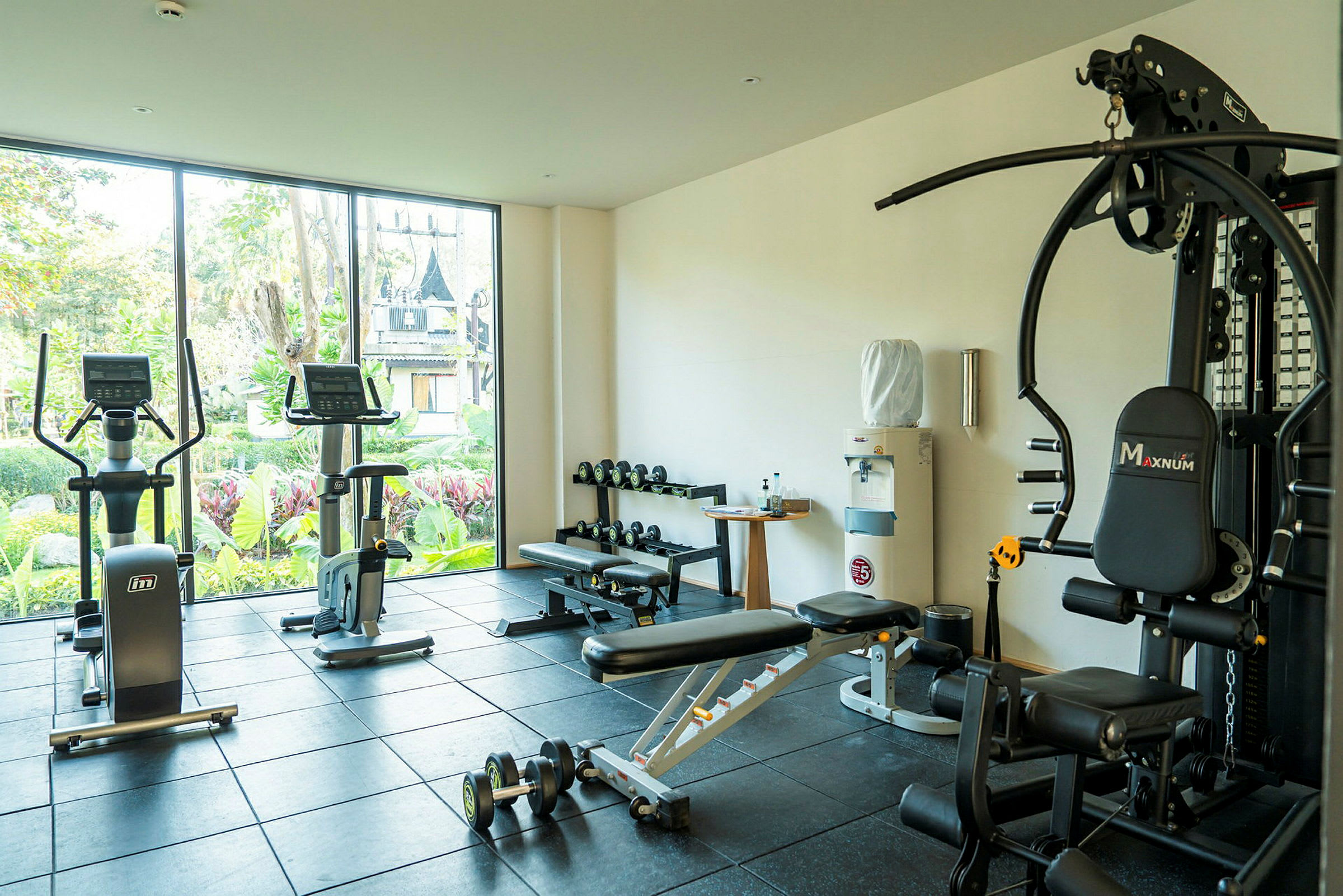 Træningsområde med fitnessudstyr og store vinduer med udsigt til frodige omgivelser. (AI-genereret tekst)