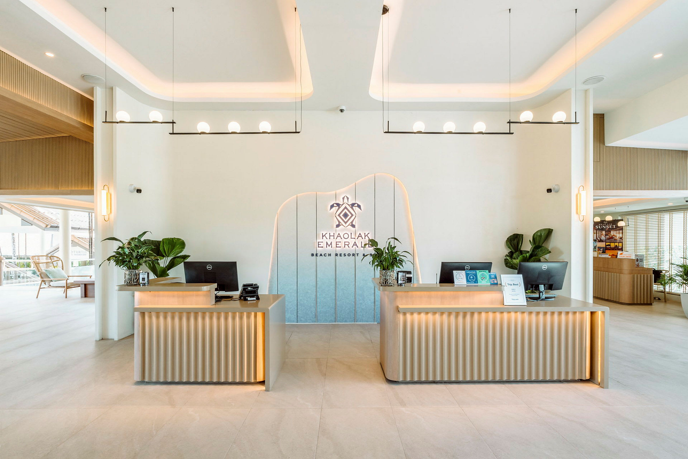 Receptionområde med to moderne skriveborde dekoreret med planter. En logo med teksten 'Khao Lak Emerald Beach Resort' er placeret på væggen. (AI-genereret tekst)