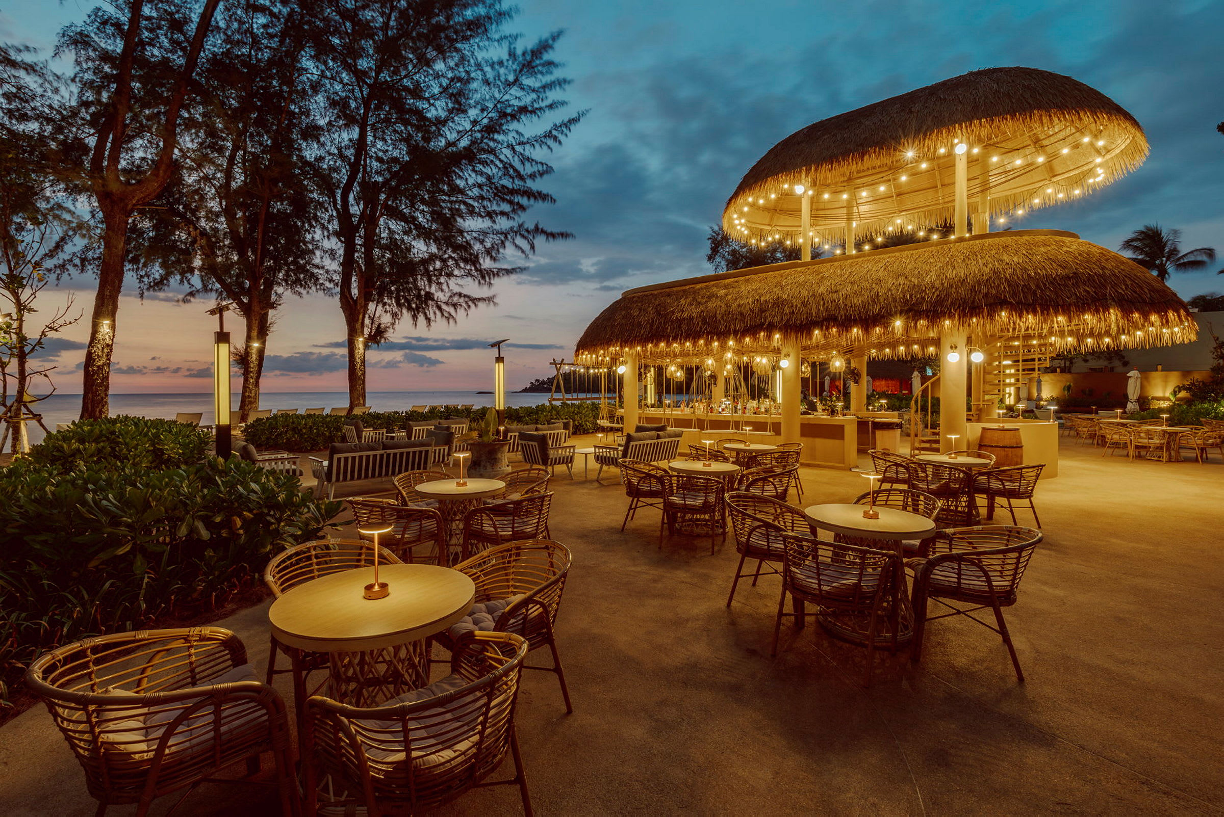 Billede af en restaurant med stråtag og udendørs servering ved solnedgang. (AI-genereret tekst)