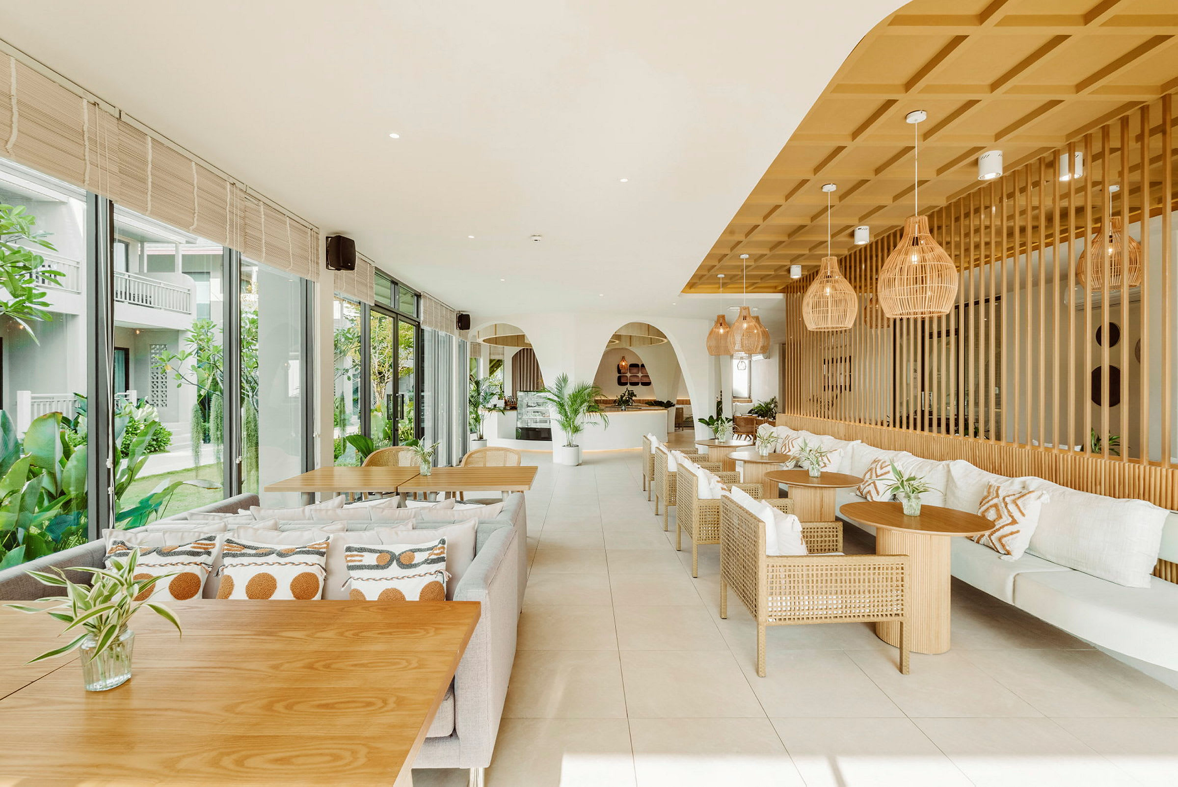 En lys og moderne restaurant med træborde og flettede stole, dekoreret med planter og indbydende puder. (AI-genereret tekst)