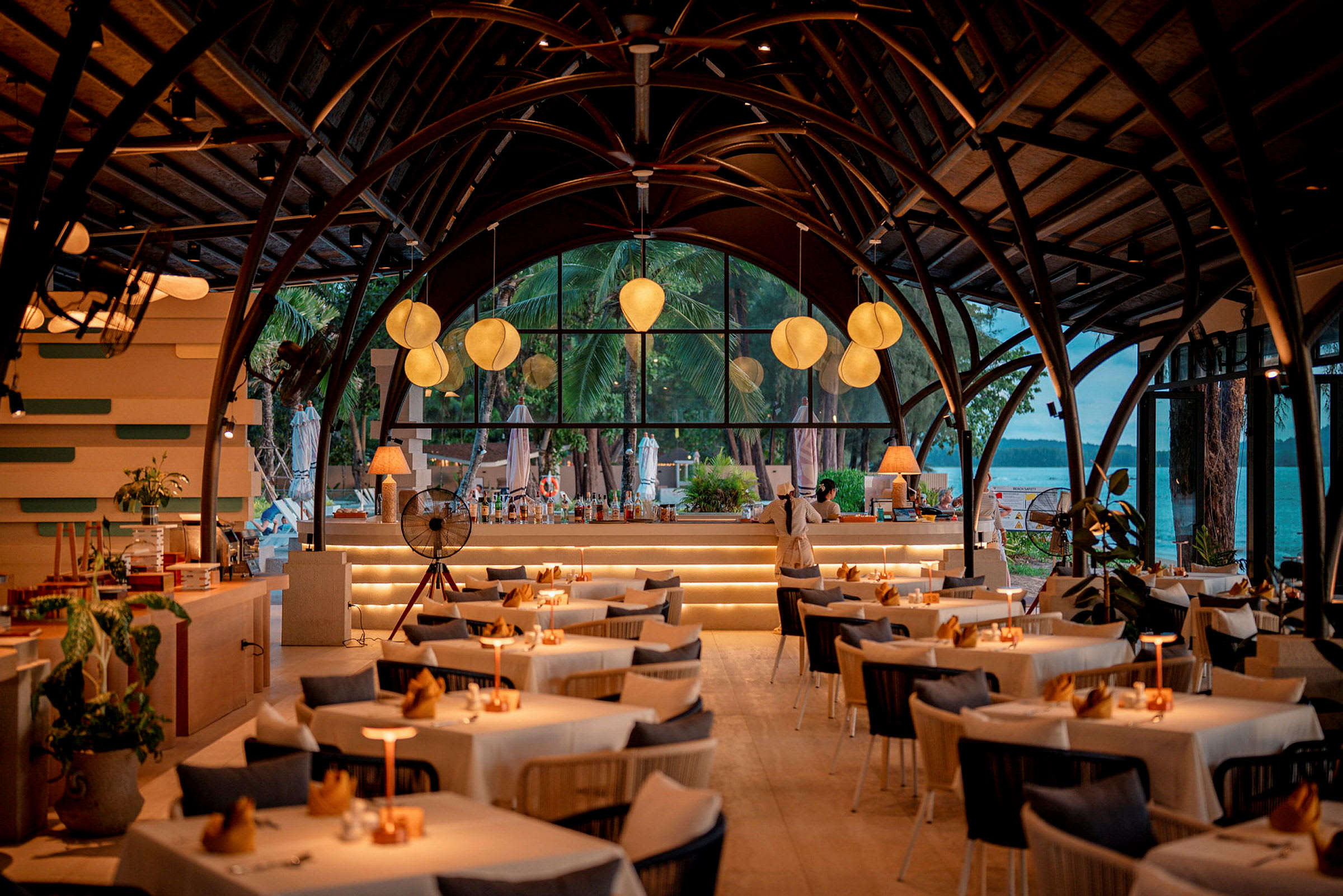 Indendørsmiljø i en restaurant med hvælvede lofter og store vinduer. Bordene er dækket med hvide duge, og omgivelserne er varmt oplyste. (AI-genereret tekst)