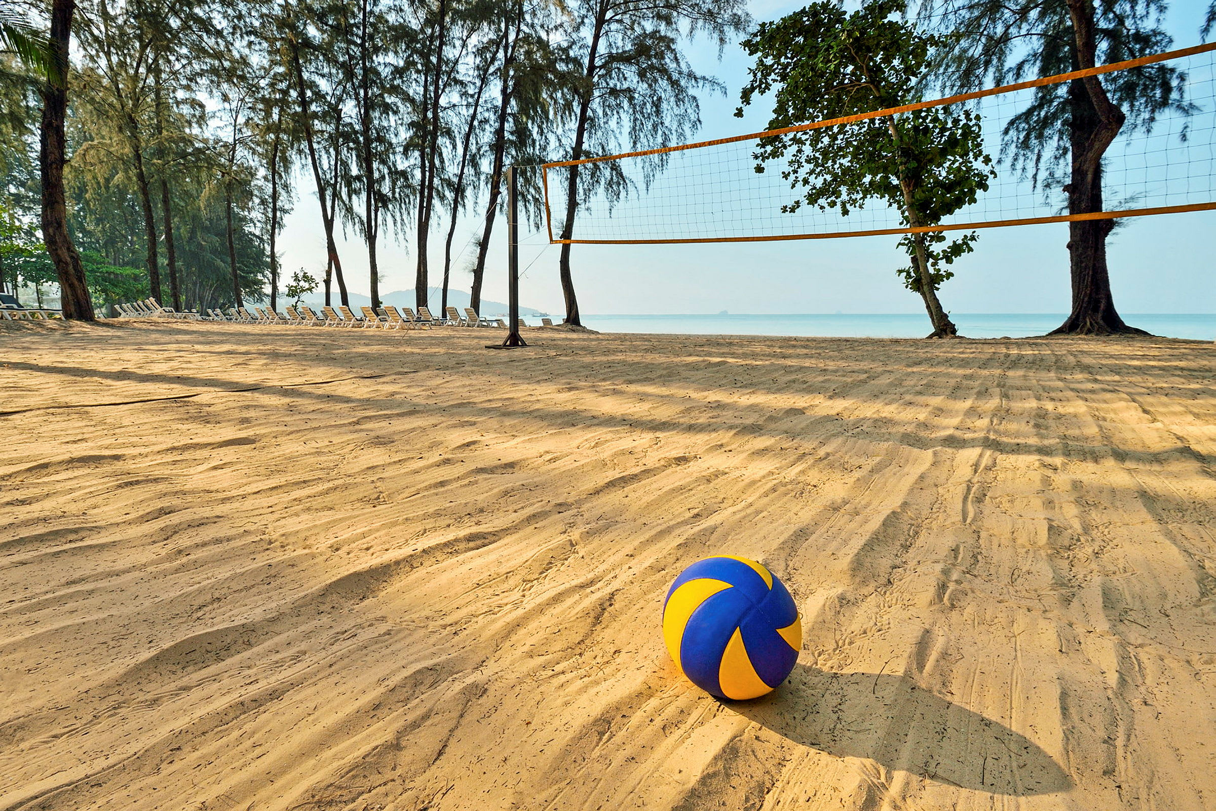En strand med et volleyballnet og en farverig volleyball i forgrunden. (AI-genereret tekst)