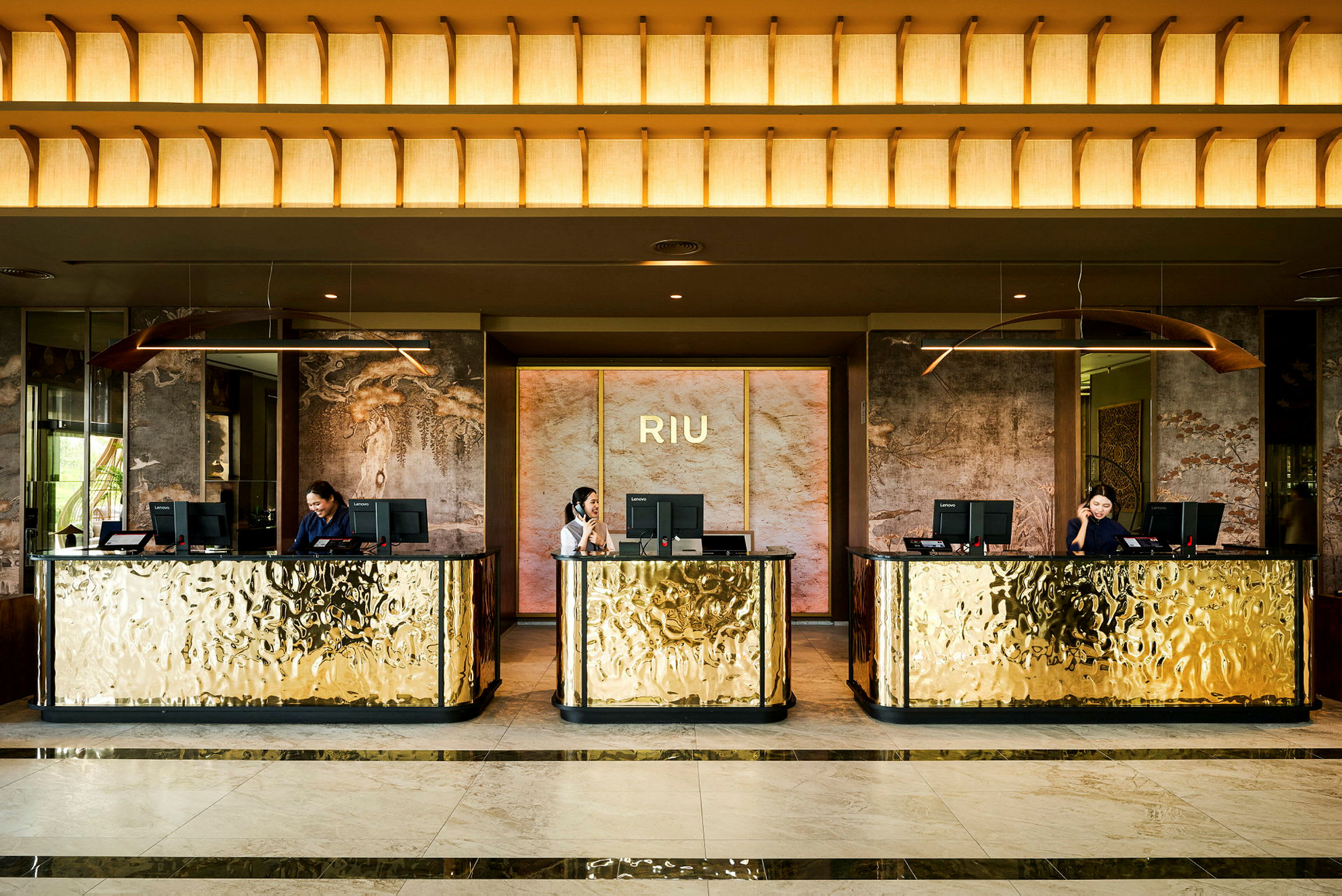 Hotelreception med tre guldfarvede skranker og receptionister. (AI-genereret tekst)