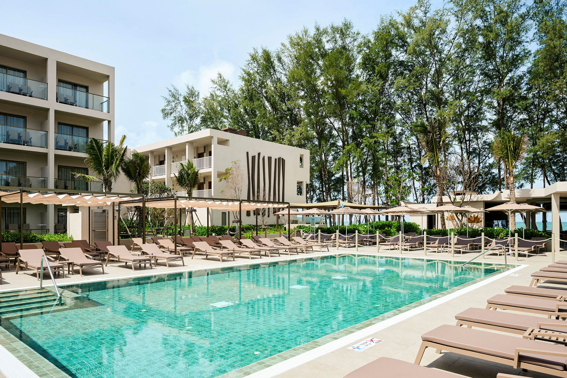 En udendørs pool omgivet af liggestole og parasoller foran et moderne hotel. (AI-genereret tekst)