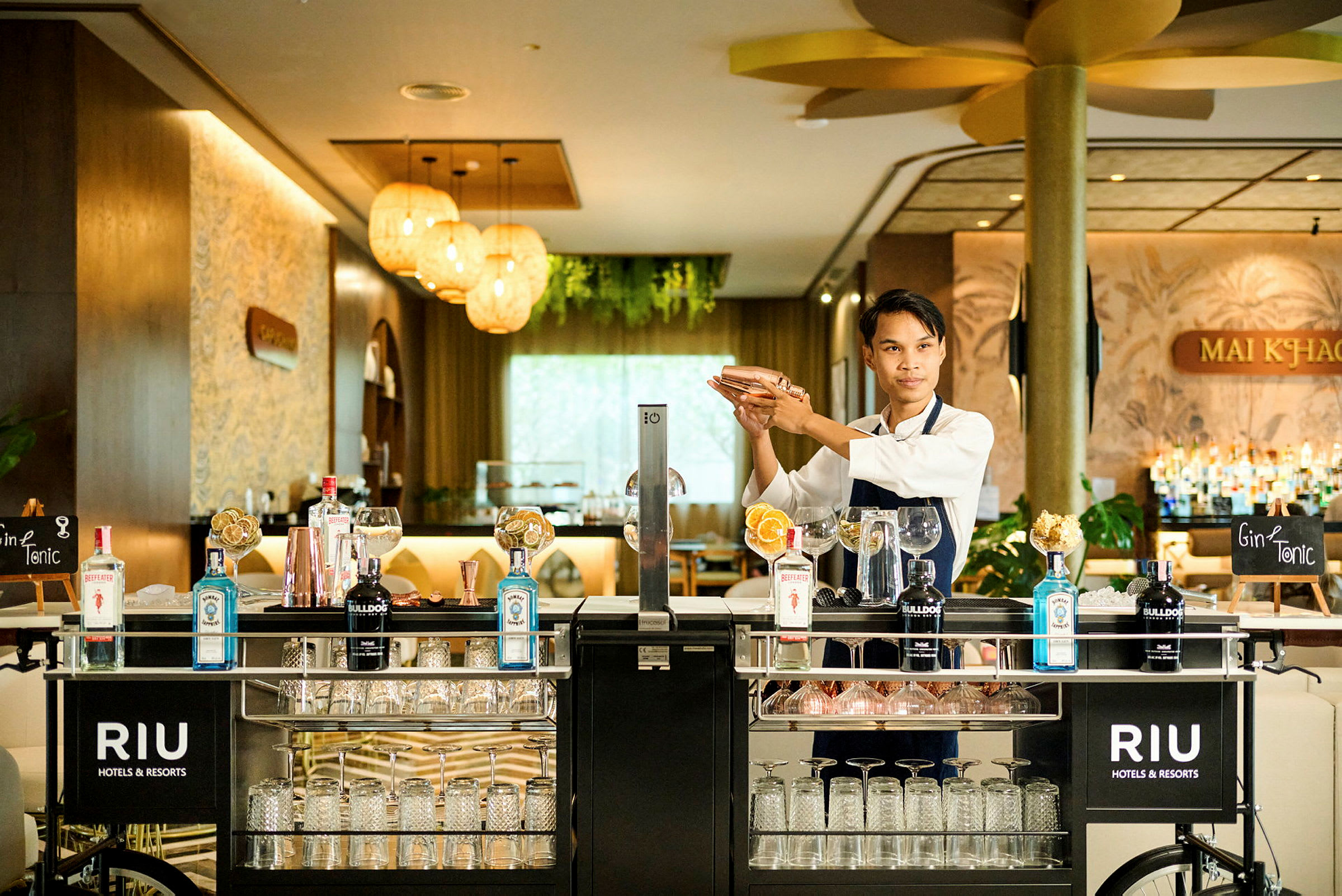 En bartender blander en drink ved en veludstyret barvogn i en elegant hotelindretning. (AI-genereret tekst)
