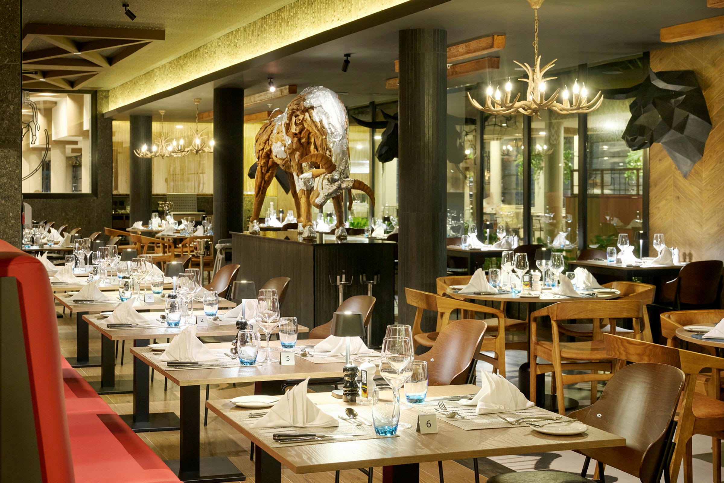 En elegant restaurant med dækkede borde og en skulptur af en bøffel i midten af rummet. (AI-genereret tekst)