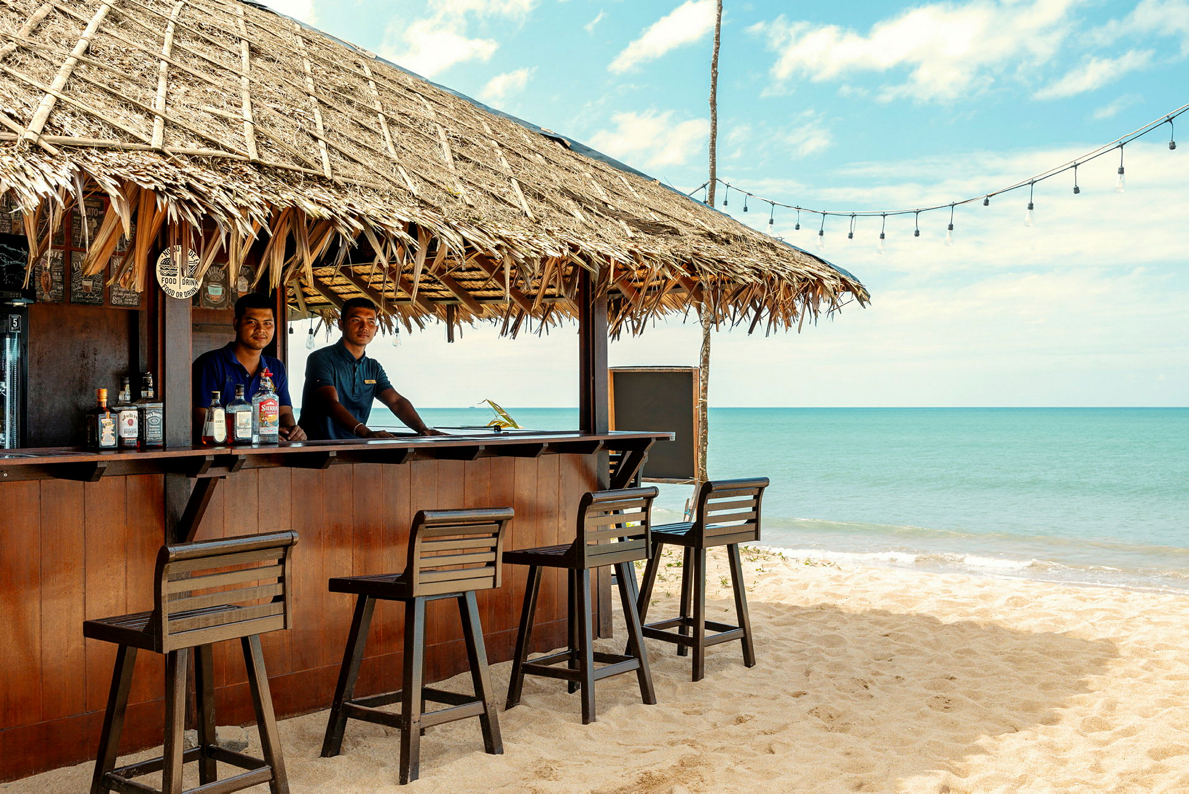 Strandbar med stråtag og hav i baggrunden. (AI-genereret tekst)
