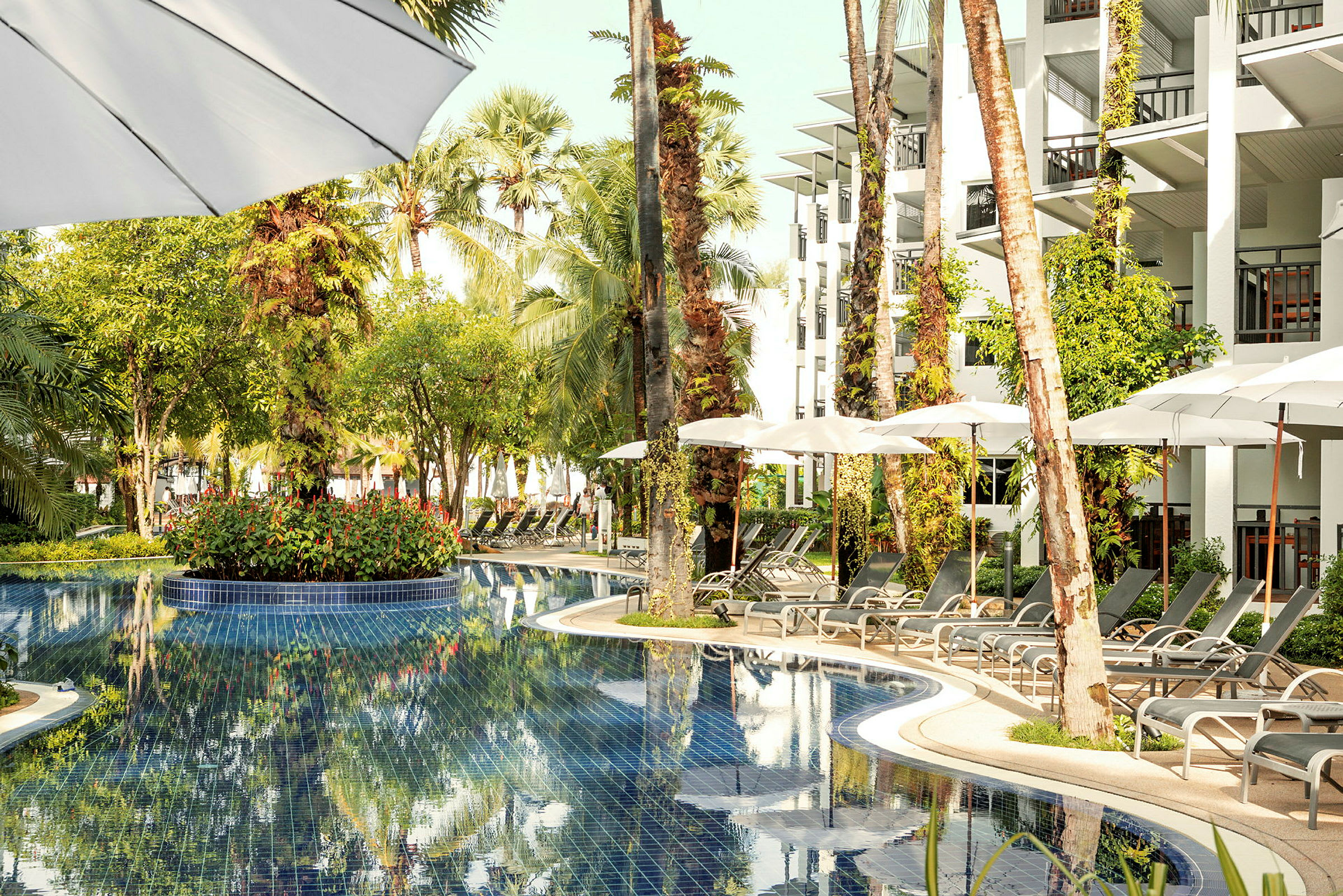 Billede af en pool omgivet af liggestole, parasoller og planter ved hotelbygningen. (AI-genereret tekst)