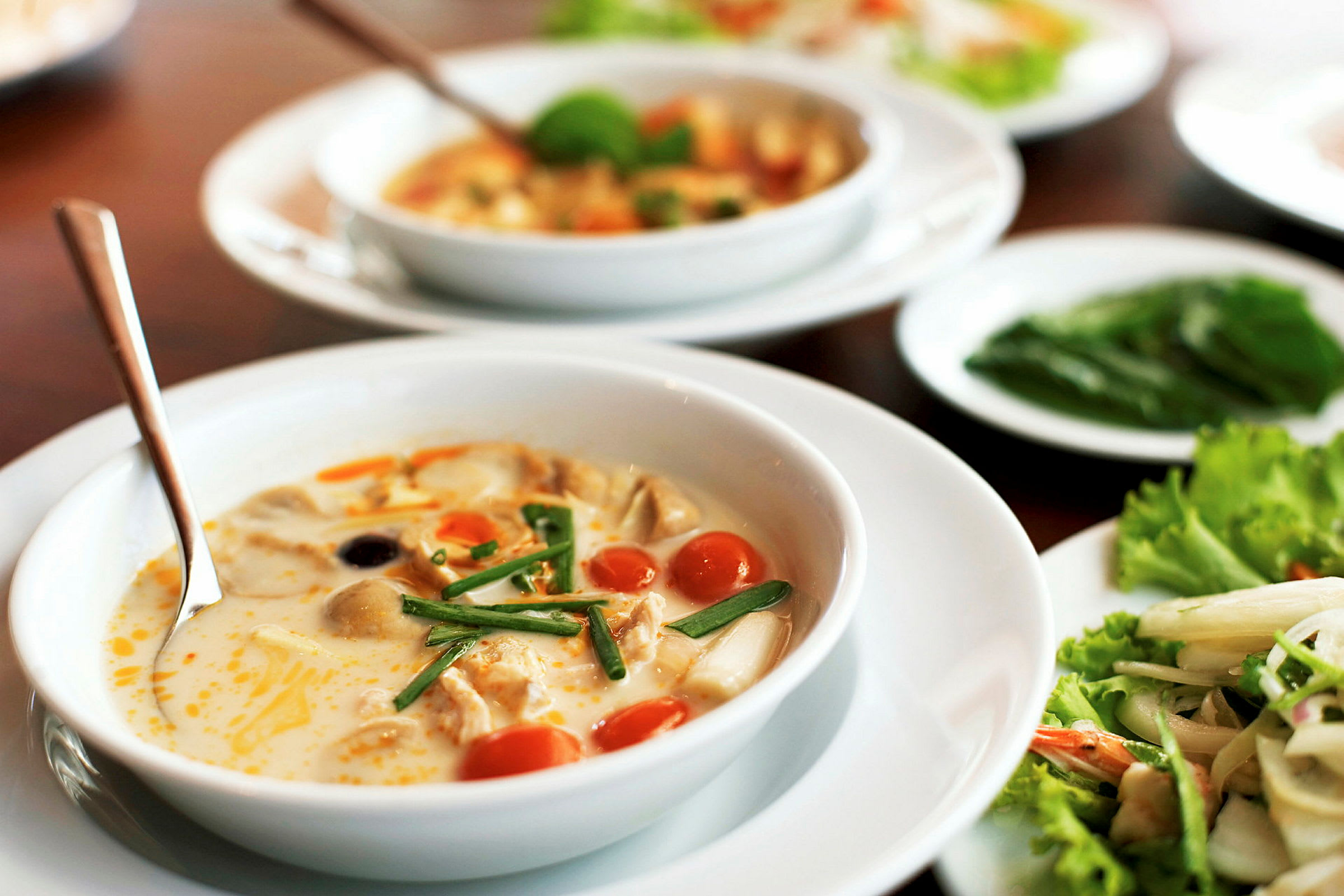 Hvid skål med suppe, der indeholder grøntsager og krydderurter, på et bord. (AI-genereret tekst)