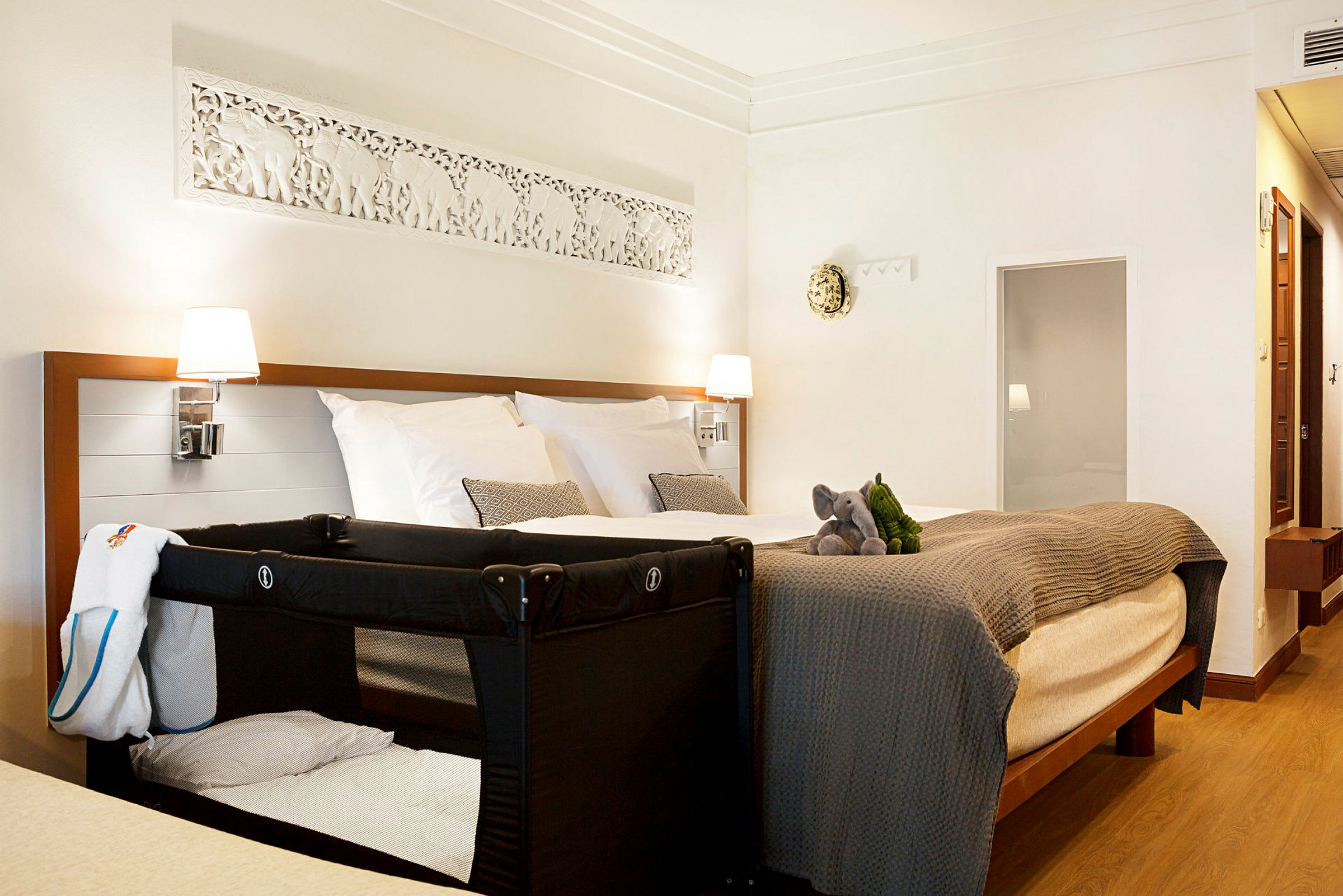 Hotelværelse med en dobbeltseng, en barneseng og to tøjdyr på sengen. (AI-genereret tekst)
