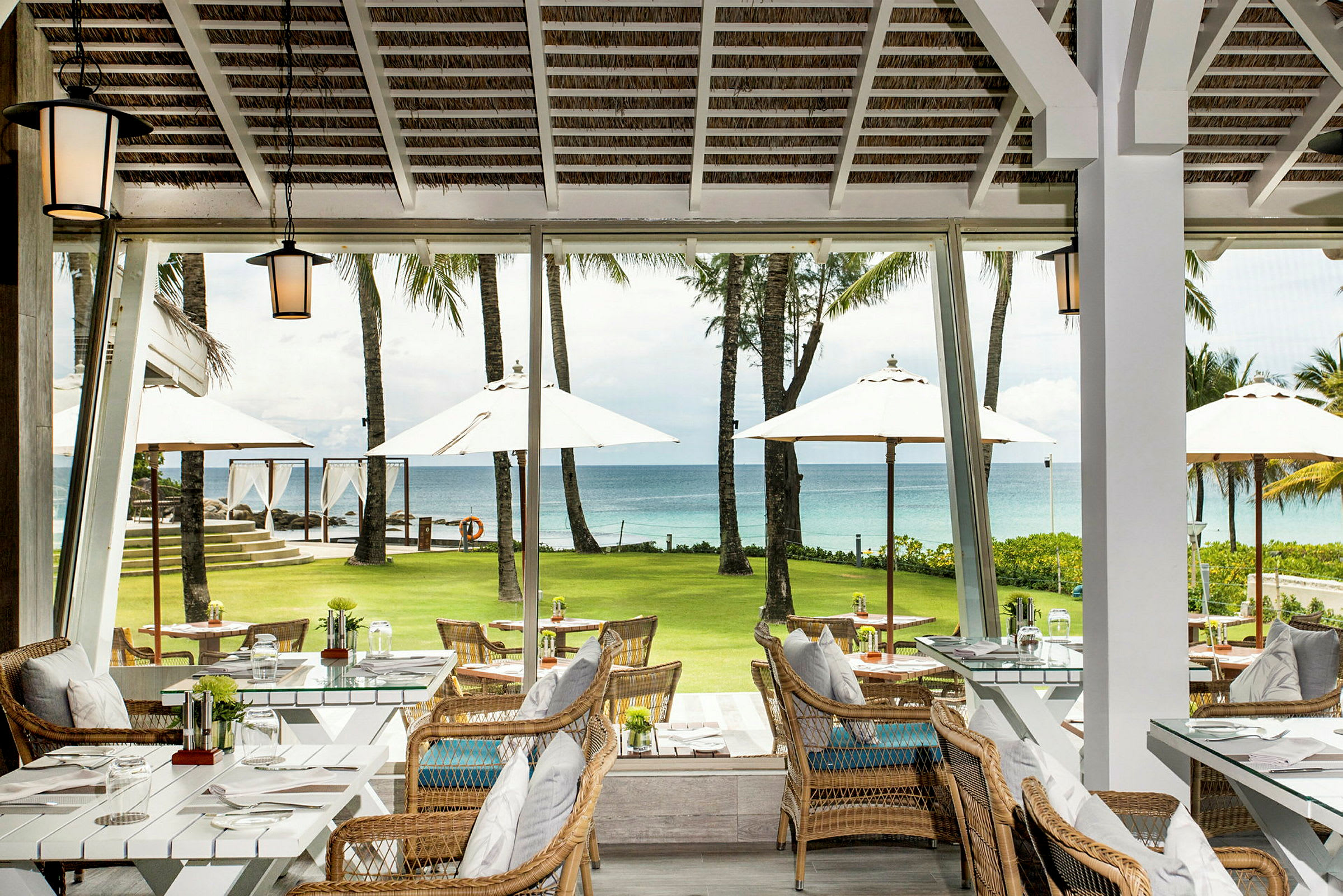 Restaurant med siddepladser og udsigt over en grøn græsplæne, parasoller og havet. (AI-genereret tekst)