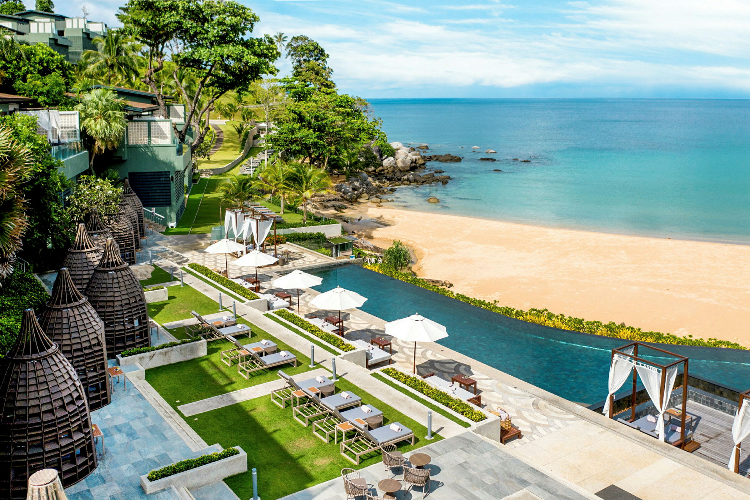 Udsigt over en infinitypool ved stranden med parasoller og vegetation. (AI-genereret tekst)