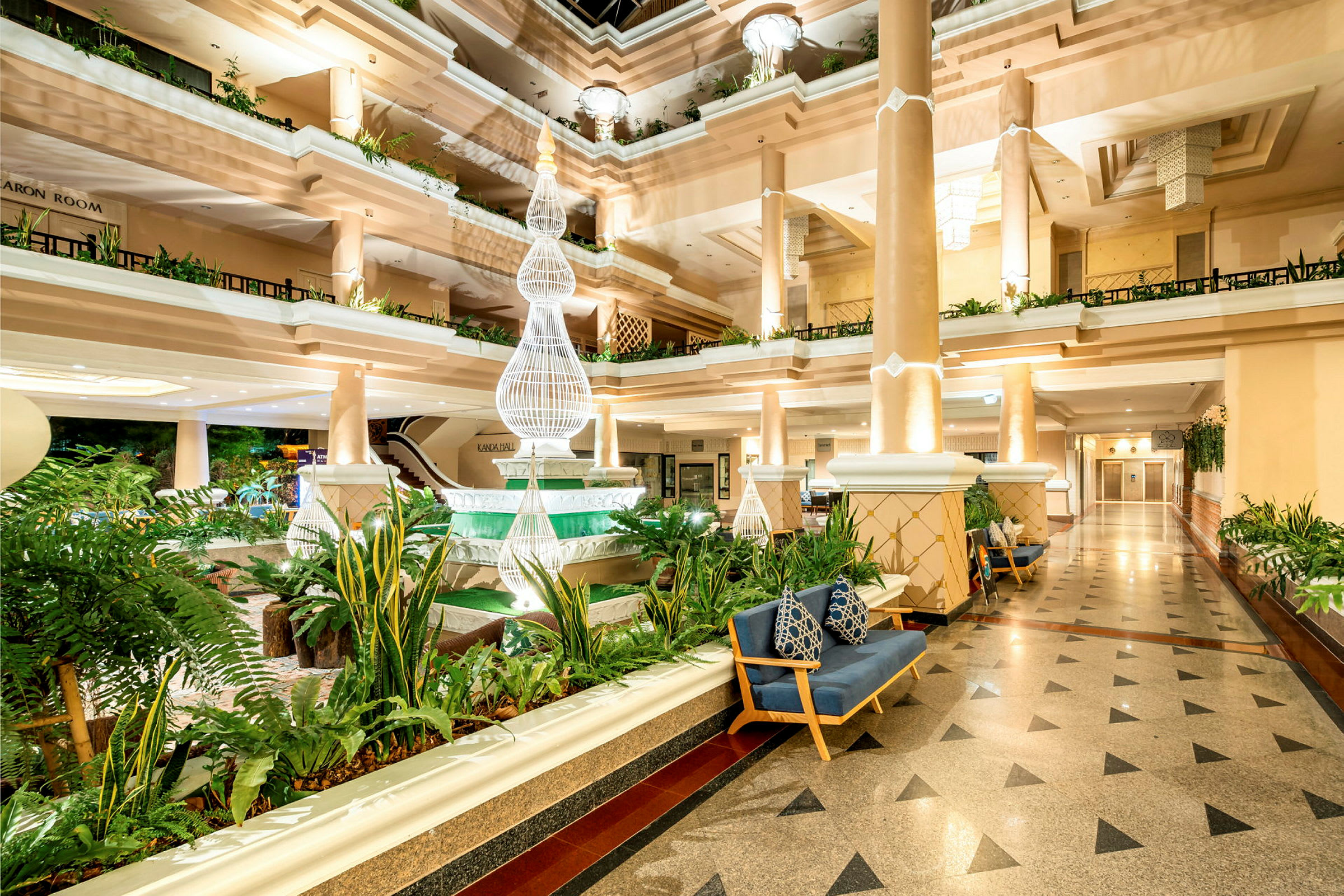 En lys og elegant hotellobby med søjler, frodige planter og dekorativ belysning. (AI-genereret tekst)
