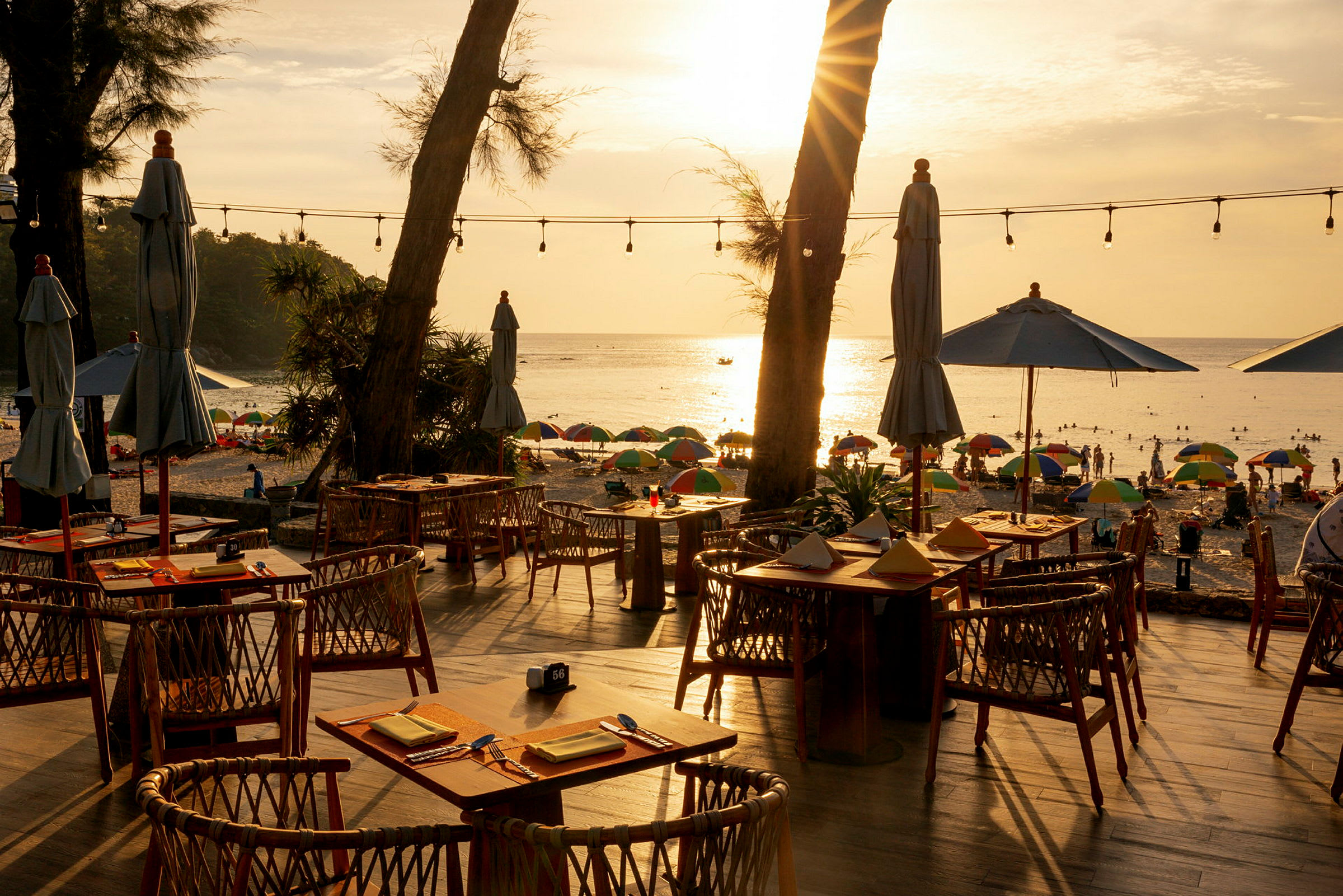 Strandnær restaurant med udendørs servering, udsigt over havet og solnedgangen. (AI-genereret tekst)