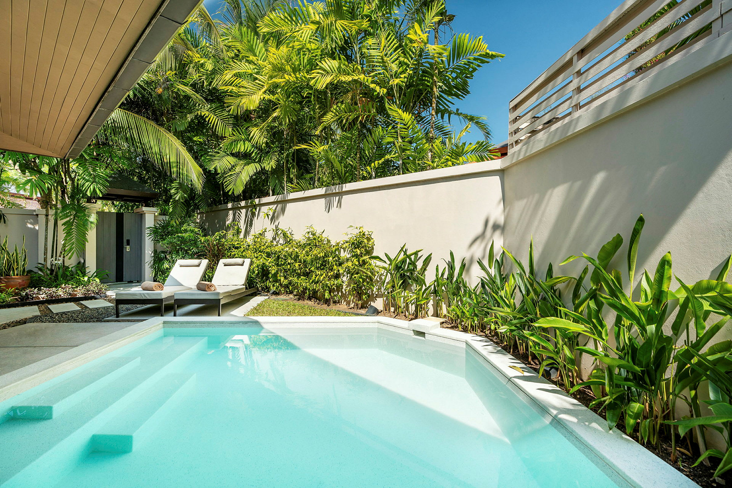 En privat pool med liggestole og omkringliggende grønne planter. (AI-genereret tekst)