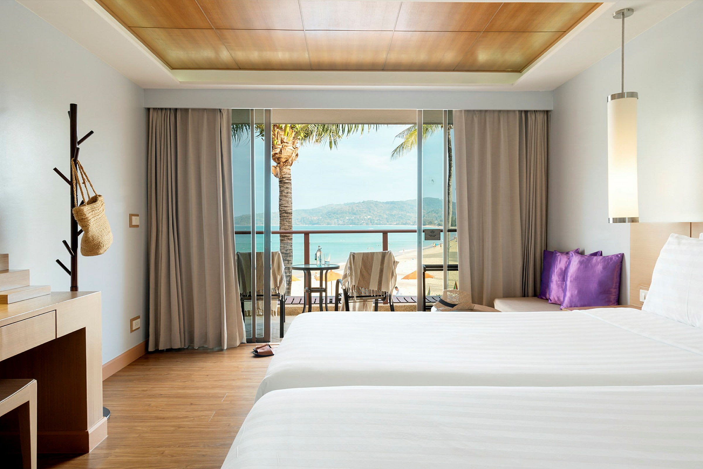 Hotelværelse med to senge, skrivebord og balkon med udsigt over stranden. (AI-genereret tekst)