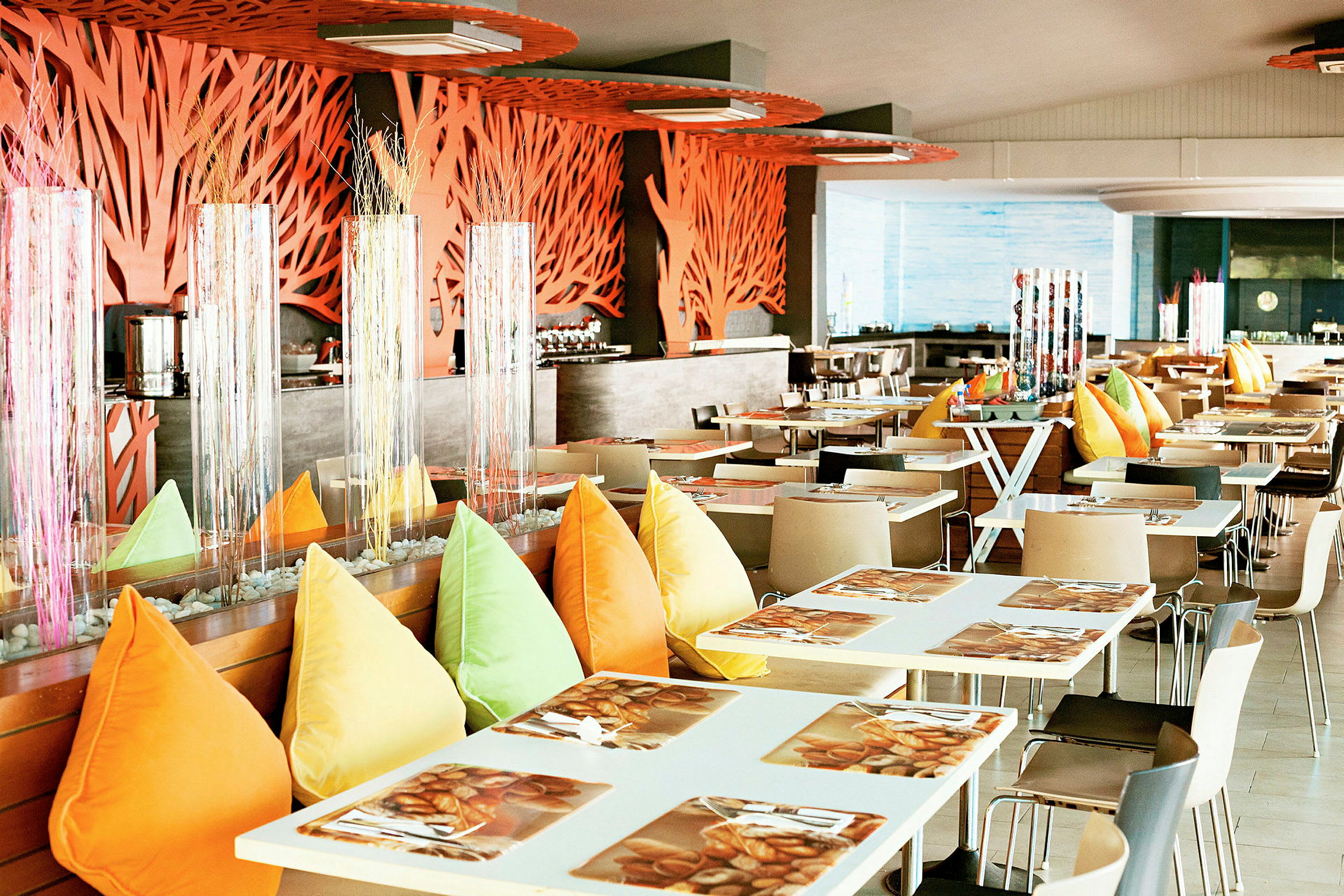 En moderne restaurant med hvide borde, farverige puder og dekorationer. (AI-genereret tekst)