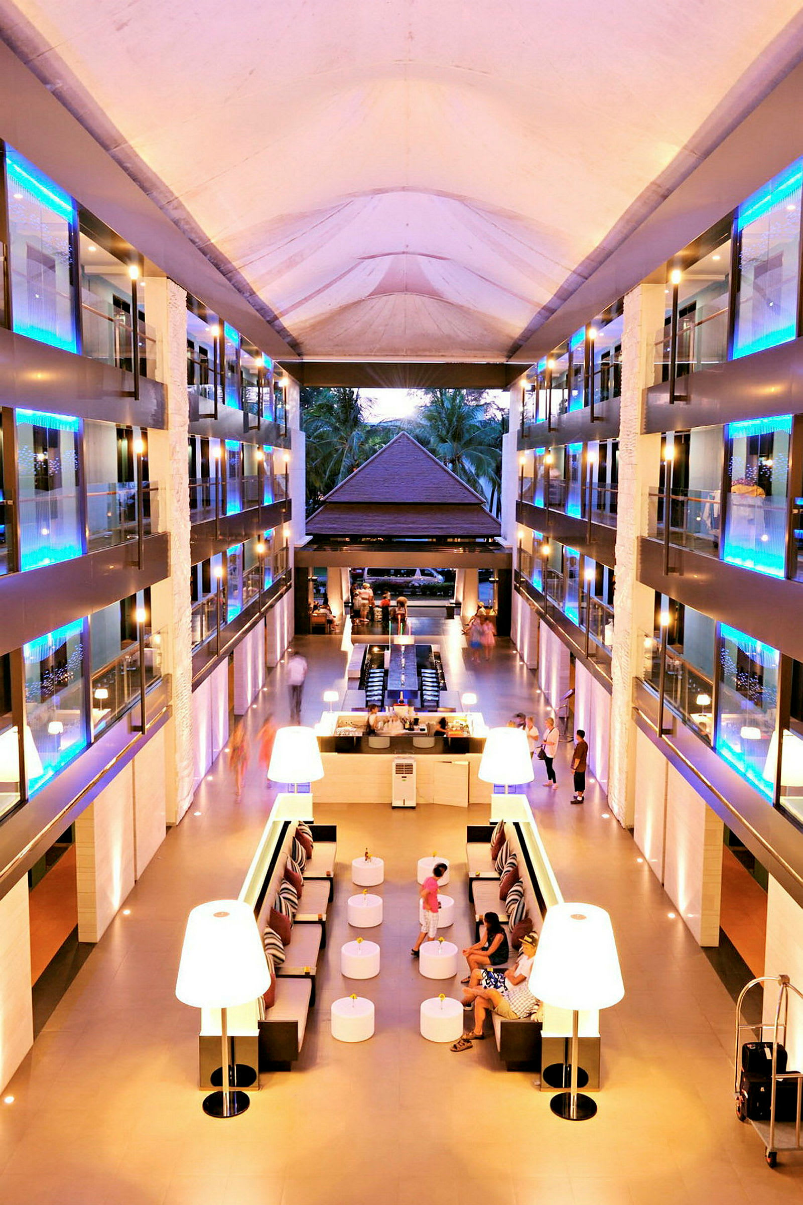 Billede af et moderne hotelatrium med siddeområder, store lamper og glaserede altaner. (AI-genereret tekst)