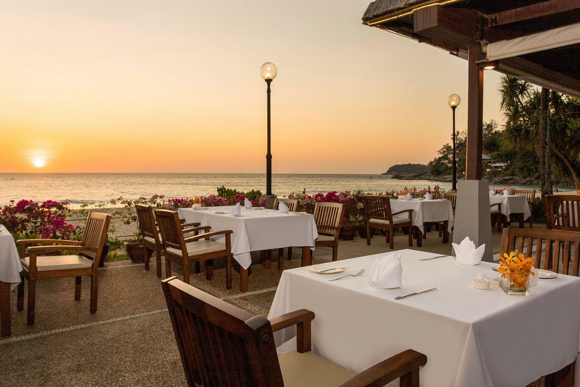 Udendørs restaurant med dækkede borde nær havet ved solnedgangen. (AI-genereret tekst)