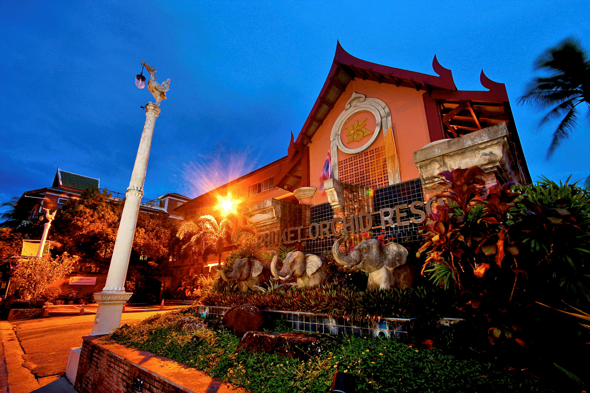 Udsiden af Phuket Orchid Resort med elefantdekorationer foran bygningen. (AI-genereret tekst)
