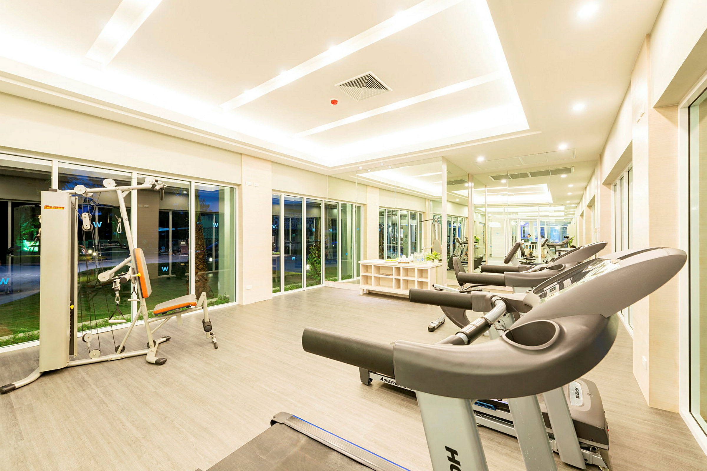 Et fitnesscenter med træningsmaskiner, løbebånd og store vinduer. (AI-genereret tekst)