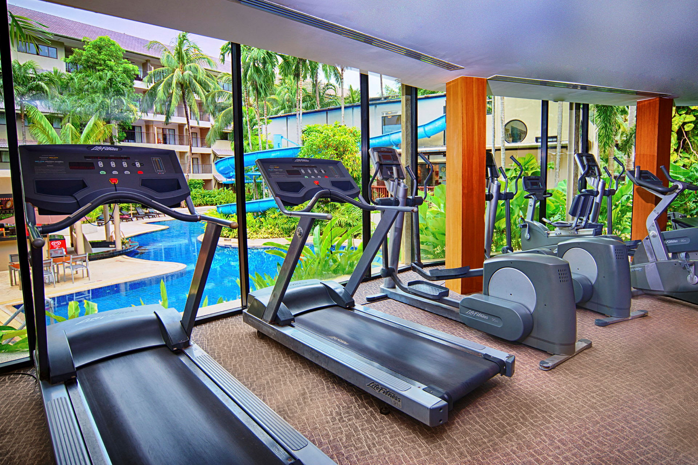 Fitnesscenter med træningsmaskiner og udsigt til en udendørs pool. (AI-genereret tekst)