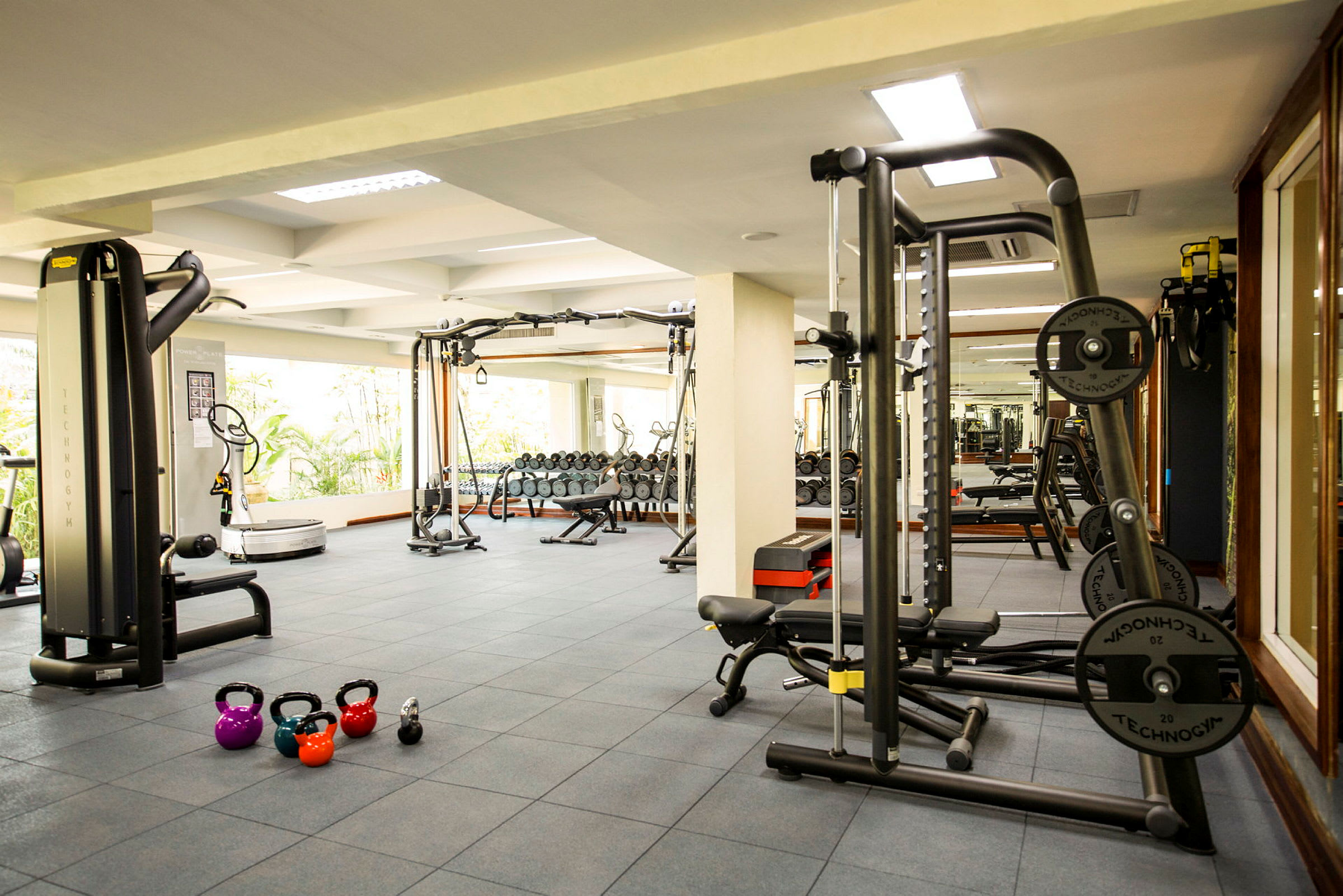 Et fitnesscenter med træningsmaskiner, håndvægte og kettlebells på gulvet. (AI-genereret tekst)