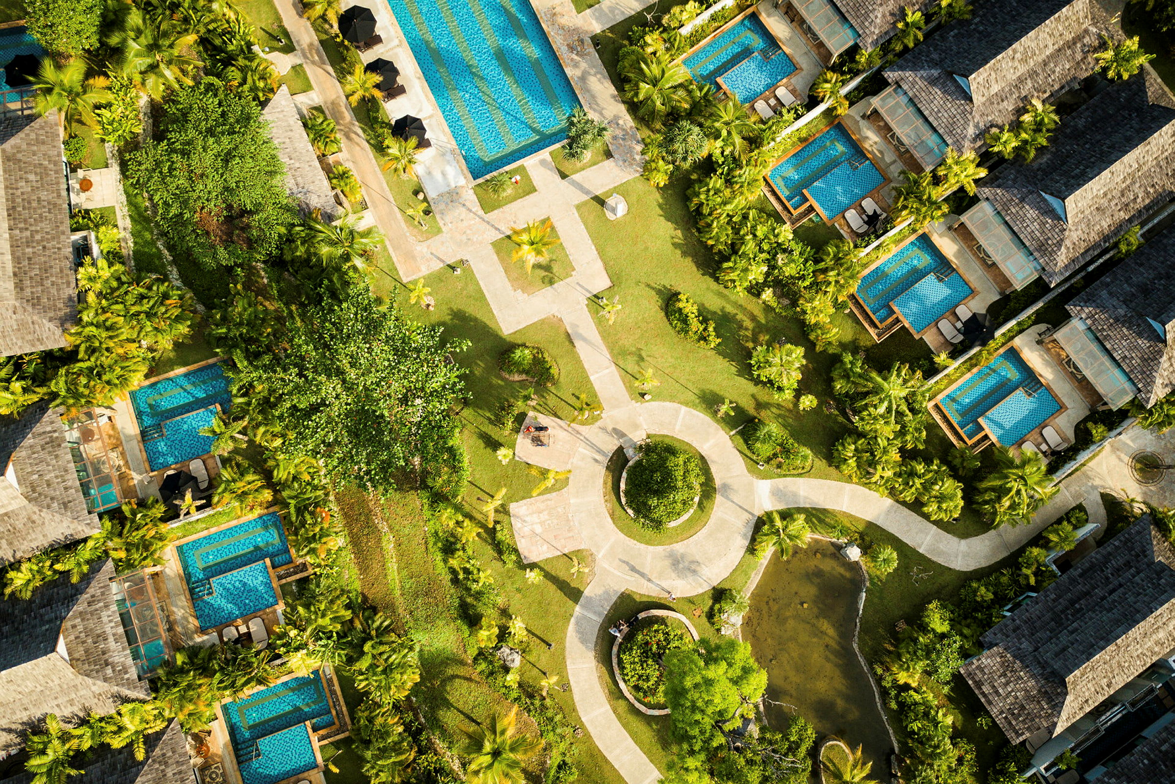 Luftfoto af et feriested med villaer omgivet af frodig beplantning og private pools. (AI-genereret tekst)