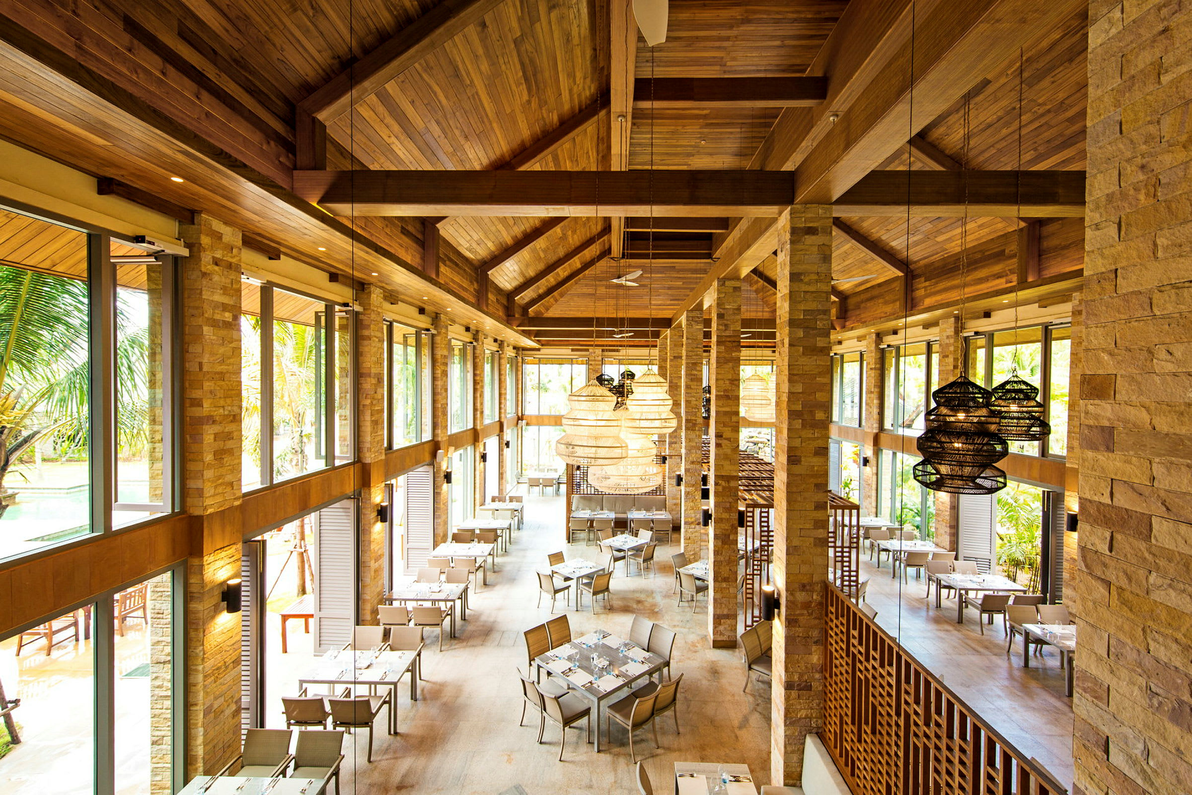 Et restaurantområde med borde og stole, store vinduer og træpaneler på vægge og lofter. (AI-genereret tekst)