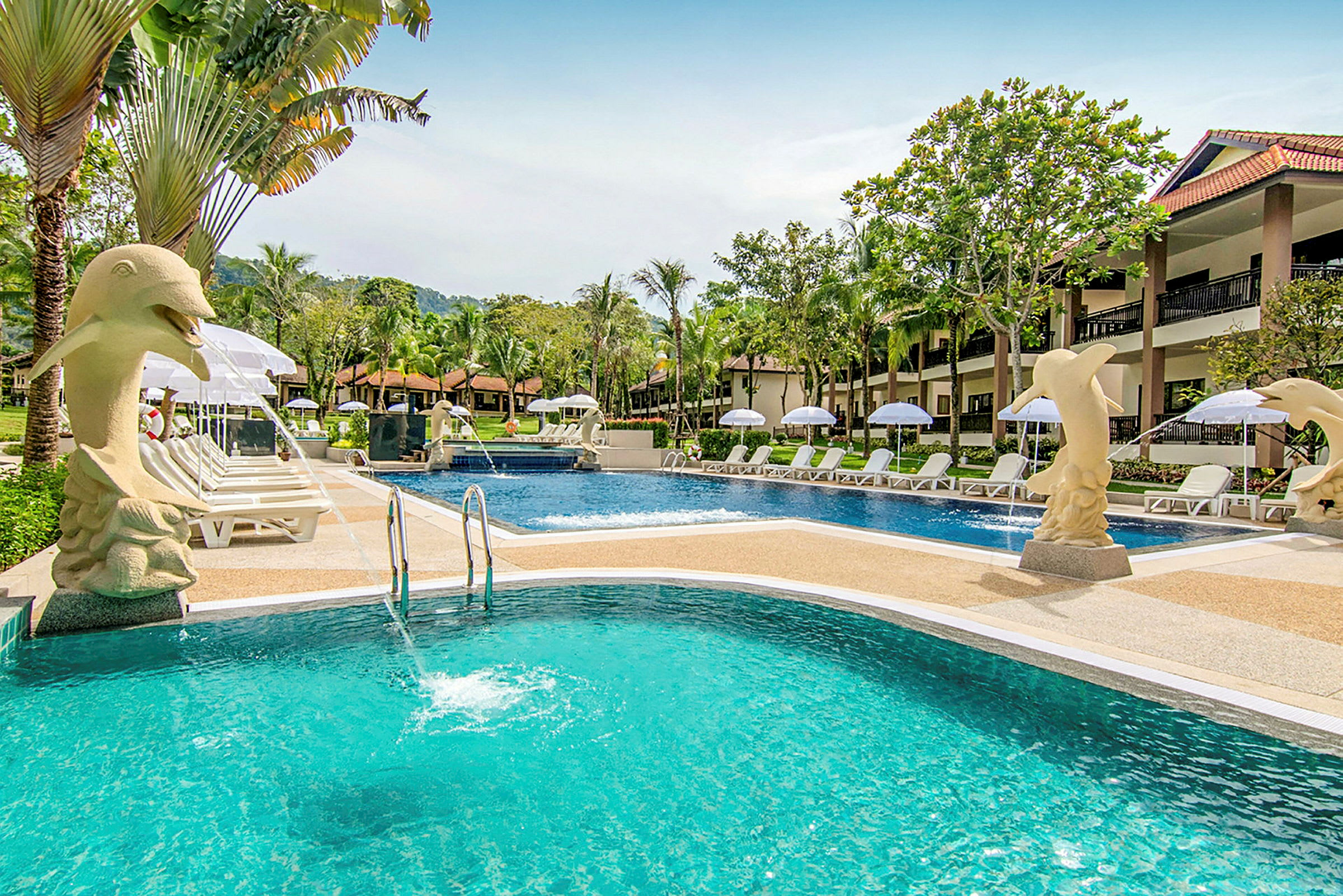 Poolområde med liggestole, parasoller samt omgivelser med have og bygninger. (AI-genereret tekst)