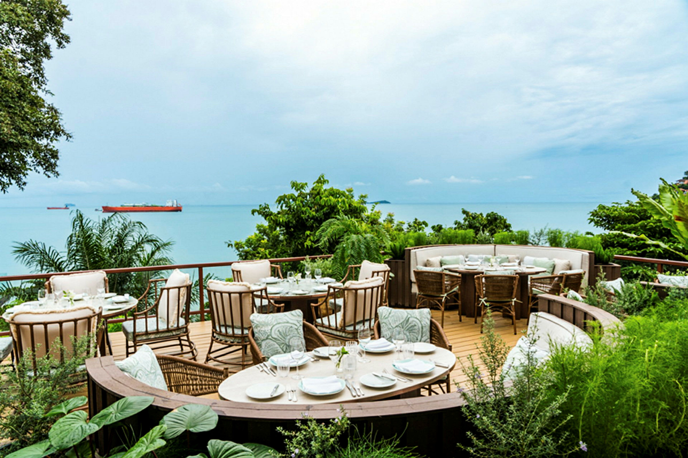 En udendørsrestaurant beliggende på en terrasse med udsigt over havet og frodigt grønt. (AI-genereret tekst)
