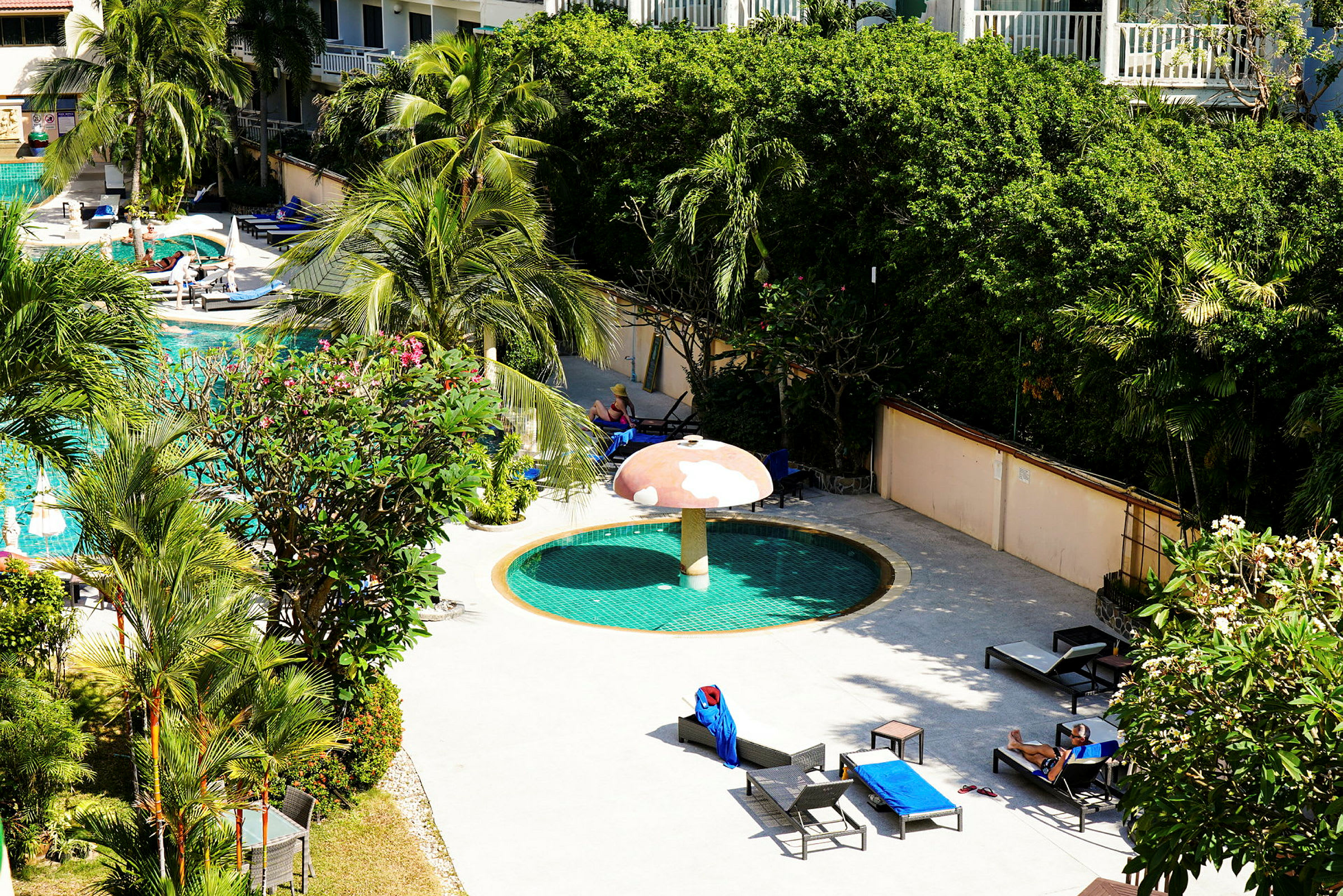 Poolområde med palmer, liggestole og en rund pool med en svampeformet parasol. (AI-genereret tekst)