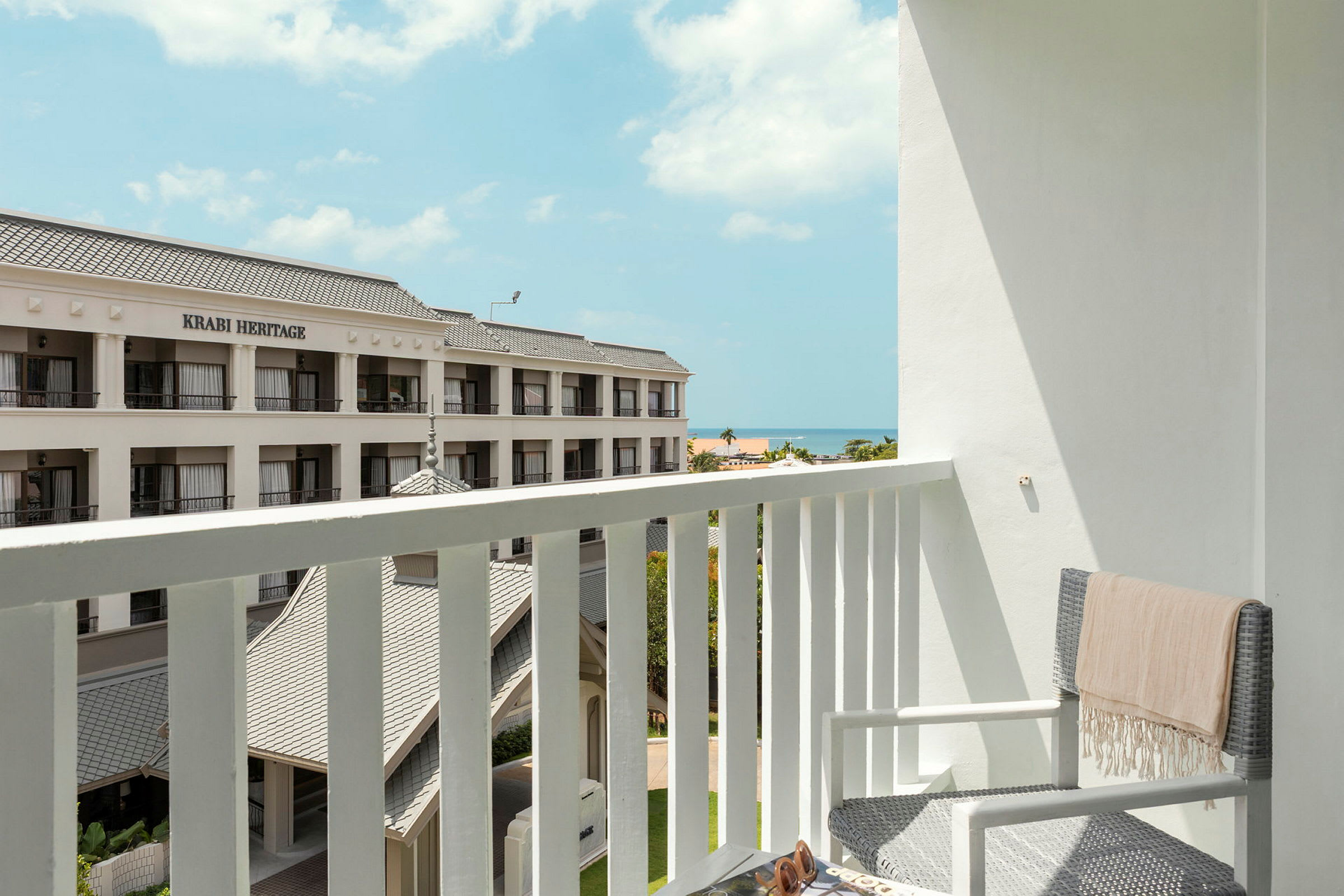 En altan med udsigt til et hotel med et skilt, der siger 'Krabi Heritage'. I baggrunden ses havet og en klar himmel. (AI-genereret tekst)