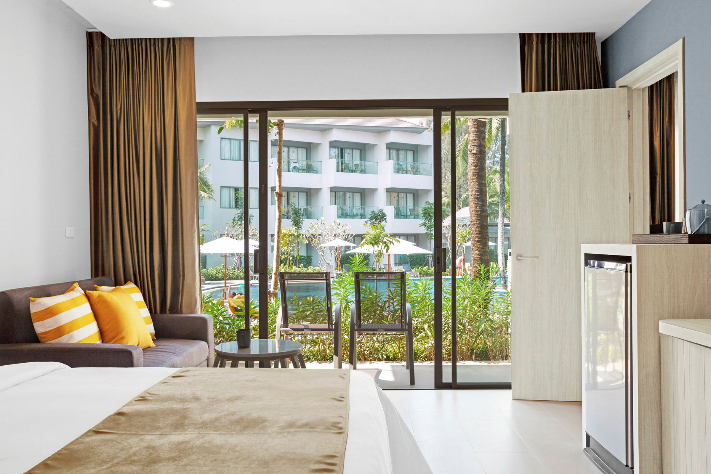 Hotelværelse med seng, sofa og balkon med udsigt til poolområde. (AI-genereret tekst)