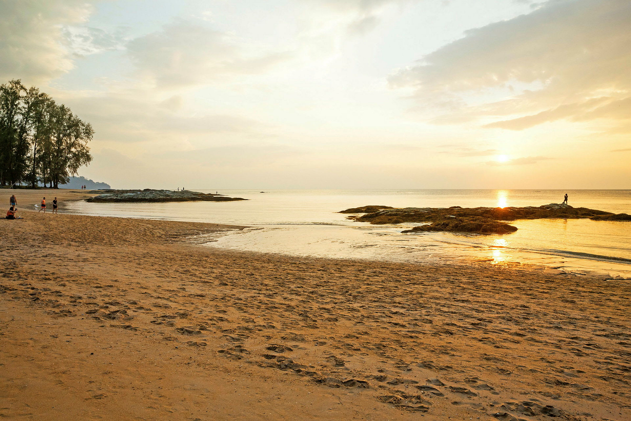 Solnedgang ved en rolig strand med nogle mennesker og sten ved vandet. (AI-genereret tekst)