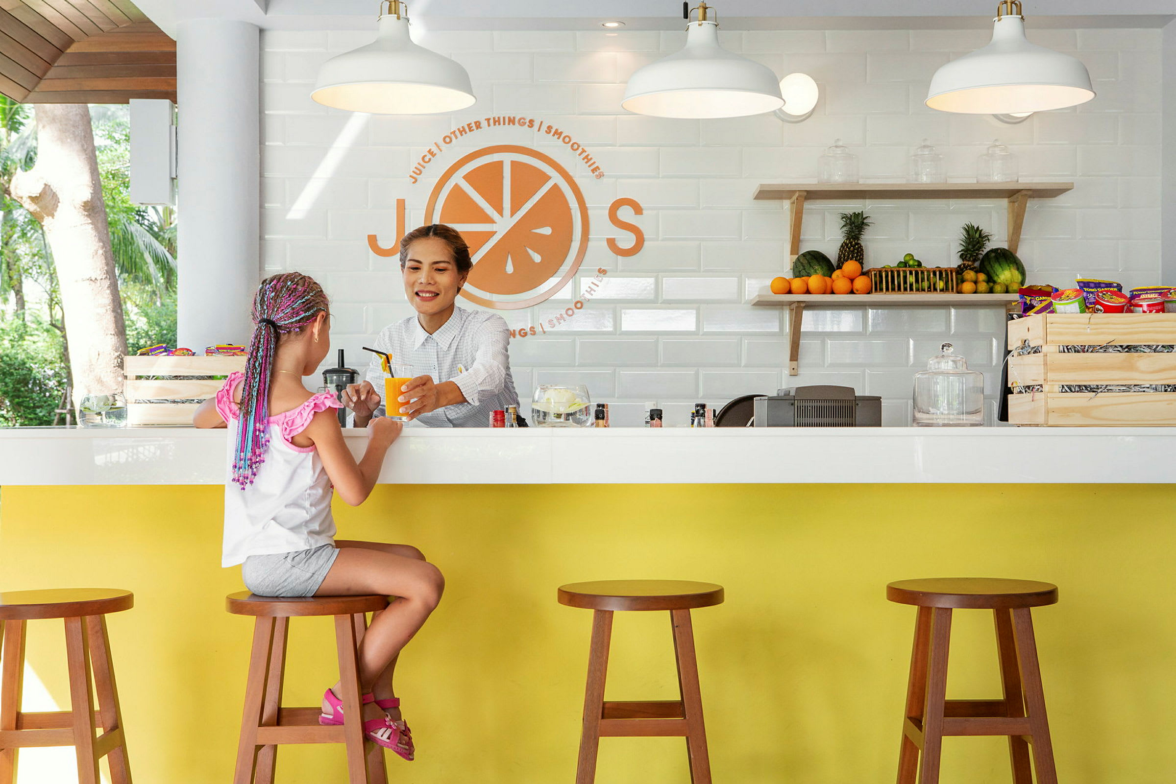 En pige sidder ved en juicebar med frisk frugt og snacks på hylden. (AI-genereret tekst)