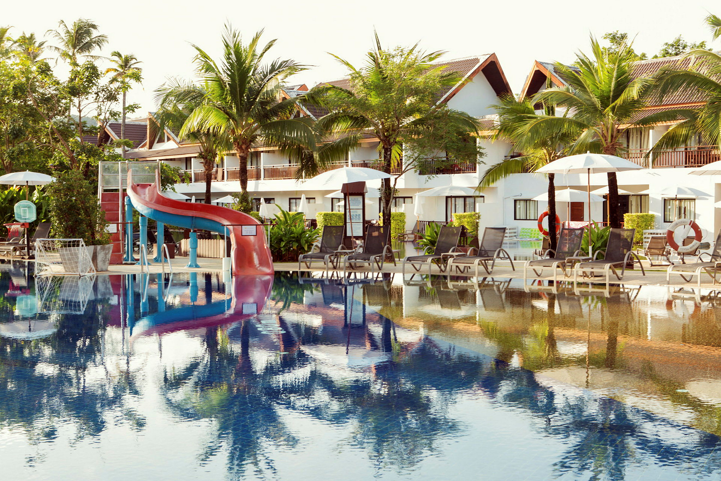 Billede af en udendørs pool ved en resort med liggestole, parasoller og en vandrutsjebane. (AI-genereret tekst)