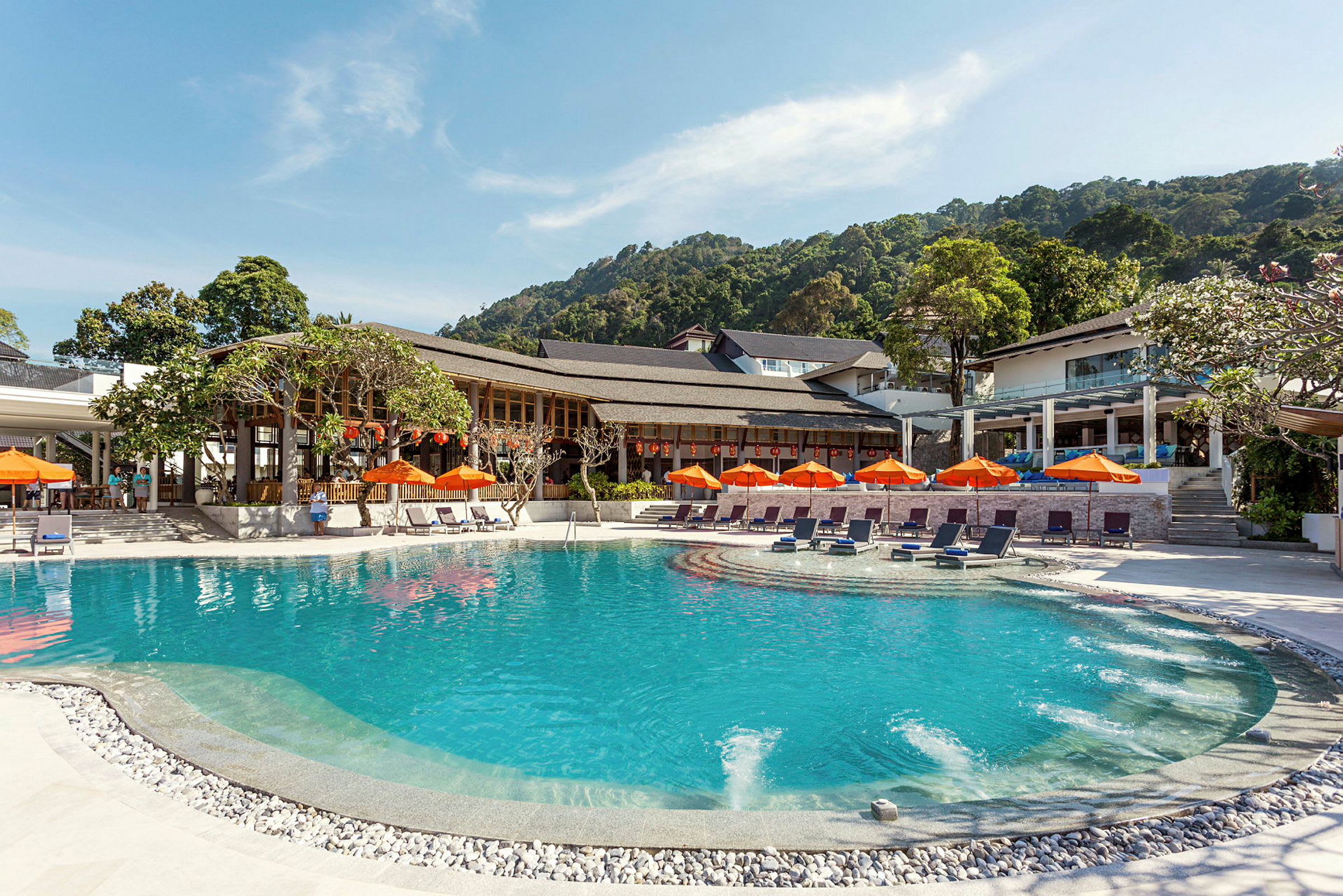 En udendørs pool omgivet af liggestole og orange parasoller, med hotelbygninger i baggrunden og frodige bakker. (AI-genereret tekst)