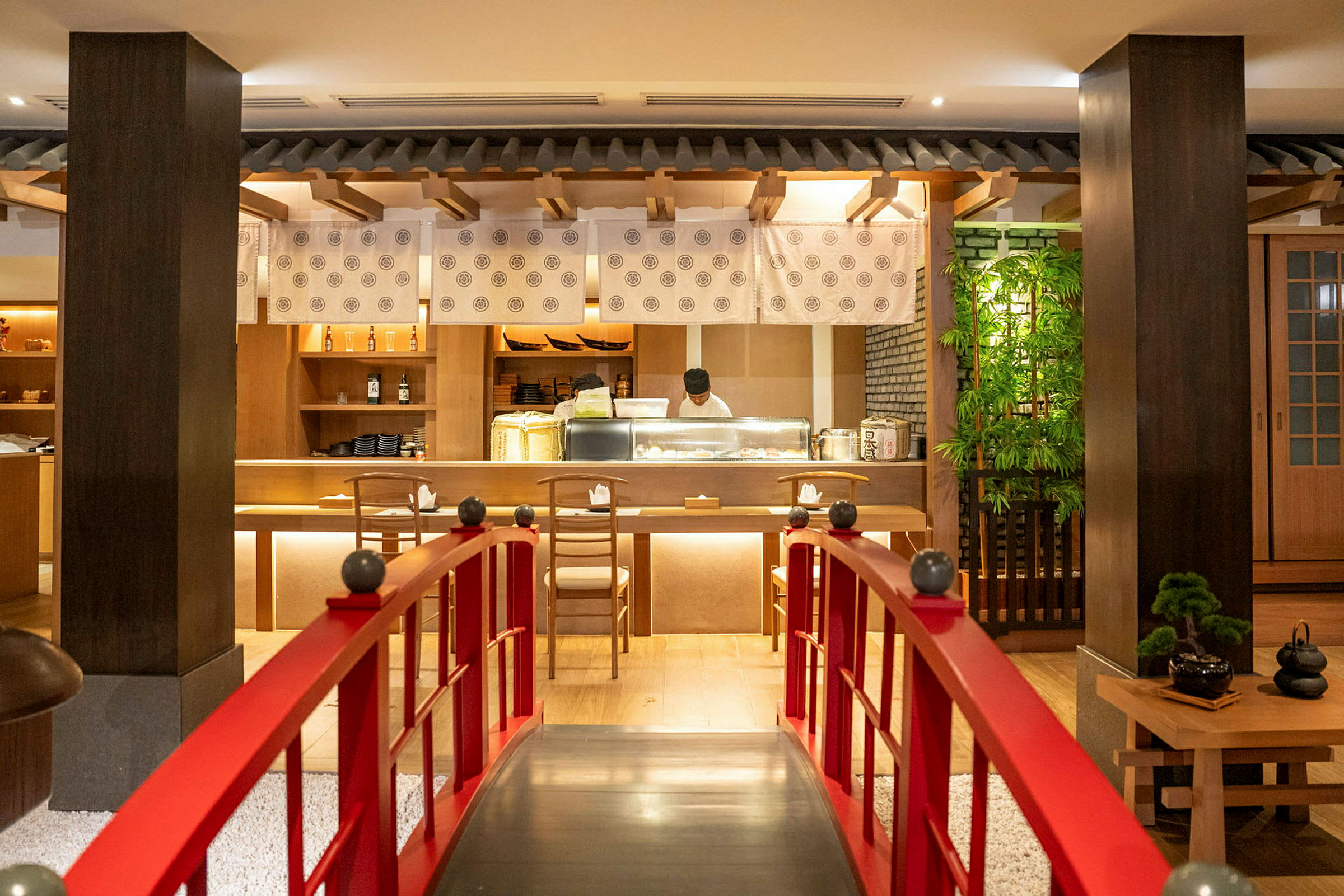 En restaurantindretning med fokus på japansk stil, en rød bro fører til en bar, hvor en kok arbejder. (AI-genereret tekst)
