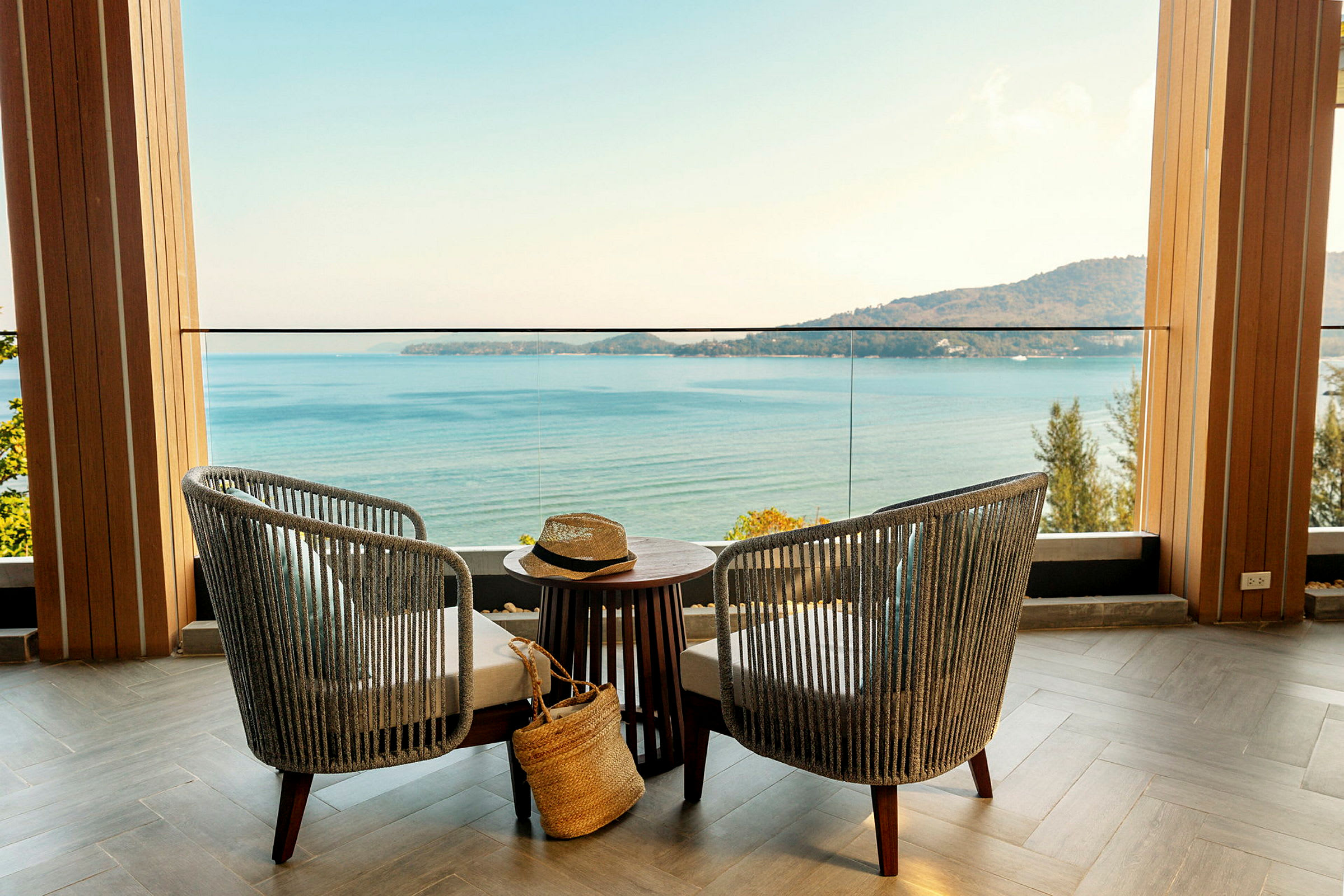 To stole og et bord står på en terrasse med udsigt over havet og en bjergkyst. (AI-genereret tekst)