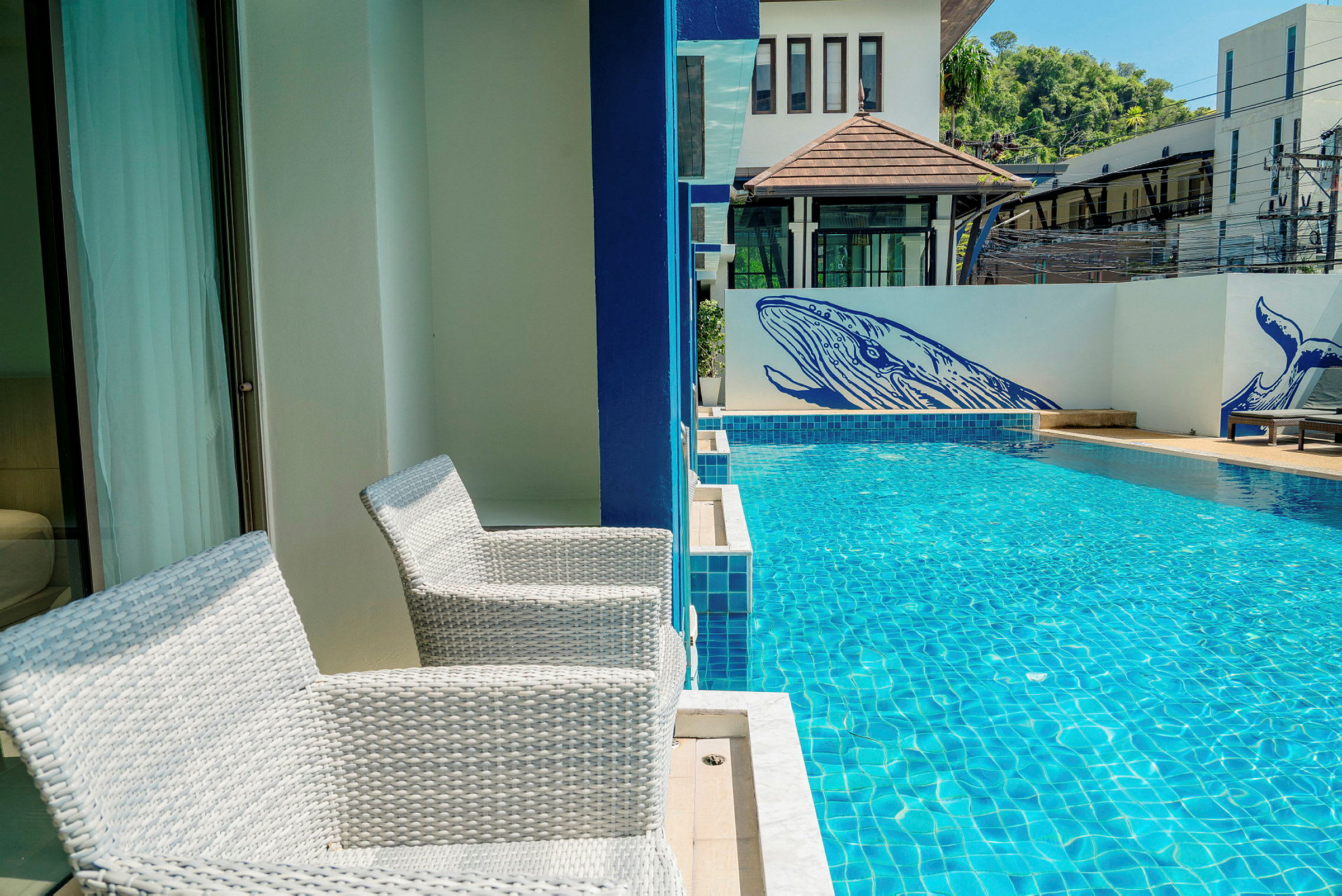 To hvide stole står på en terrasse ved siden af en swimmingpool. På væggen ved poolen er der blå malerier af hvaler. (AI-genereret tekst)