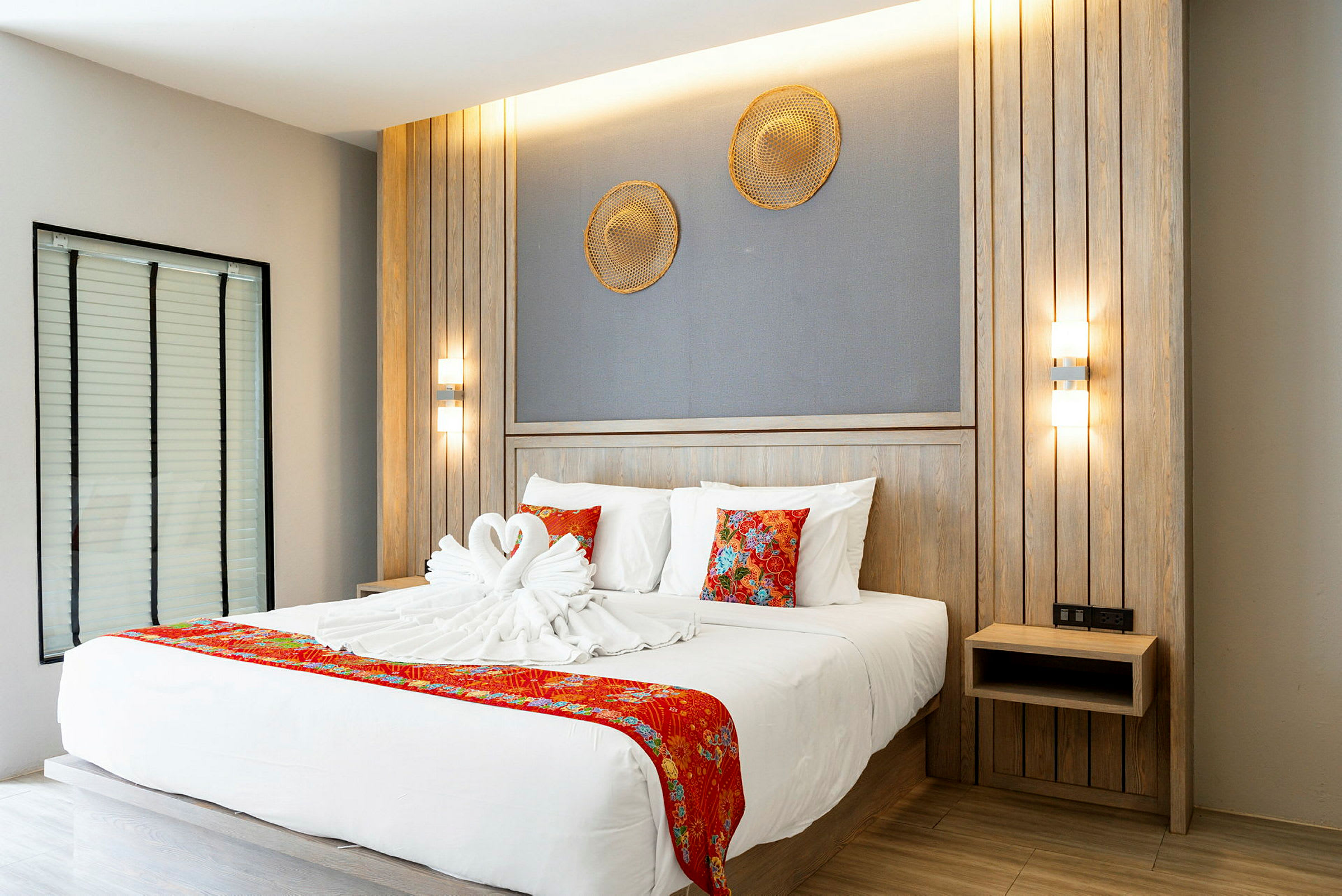Moderne hotelværelse med en dobbeltseng dekoreret med håndklæder formet som svaner og røde detaljer. (AI-genereret tekst)