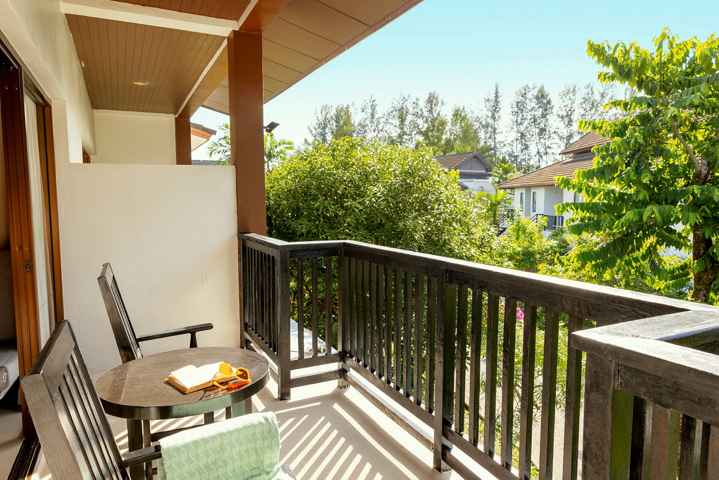 Udsigt fra en balkon med bord, stole og træer omkring. (AI-genereret tekst)